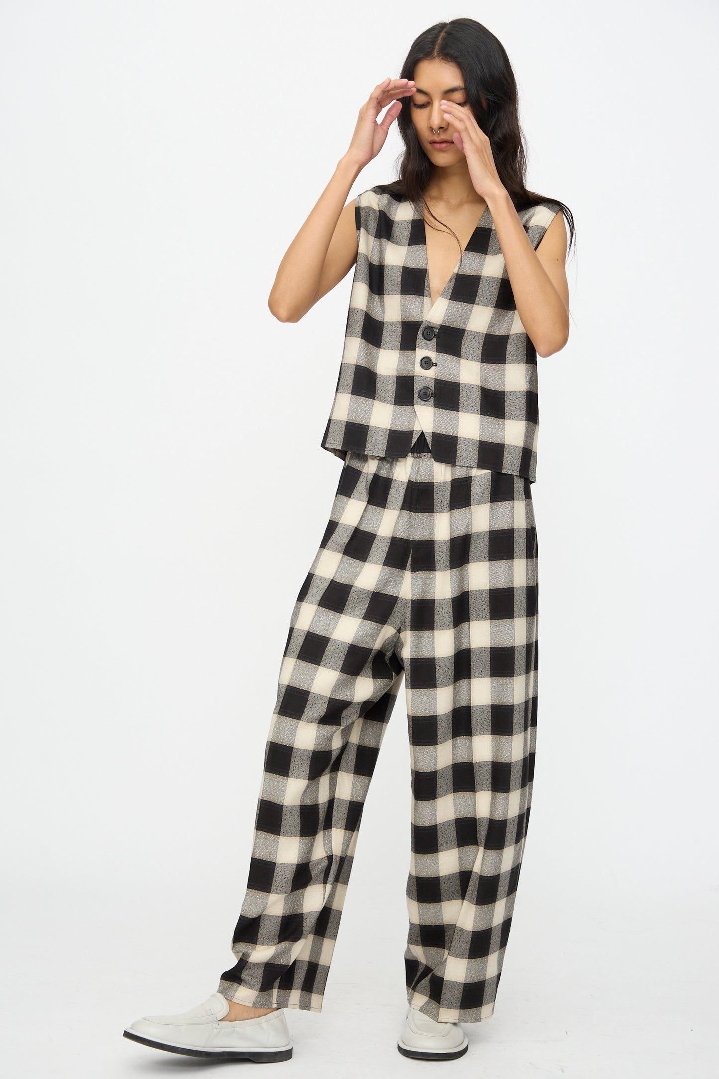 Model in Cristaseya Button Down Vest in Black and Cream Checks, paired with matching wide-leg pants and white slip-on shoes, stands against a plain white background.