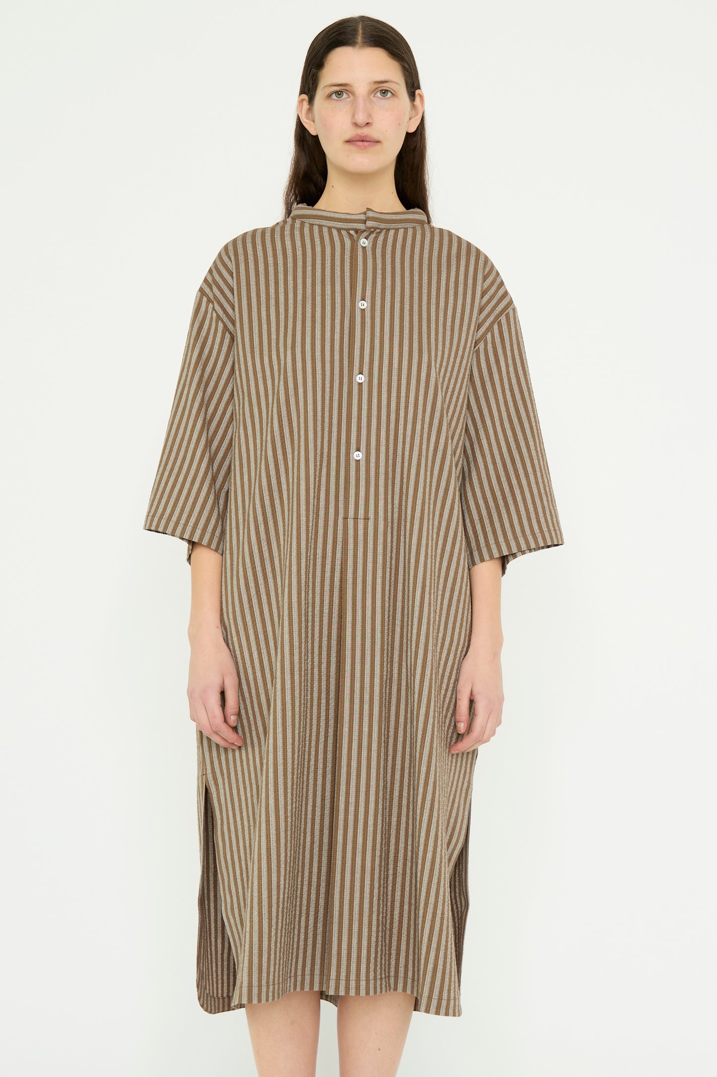 A person in the Caftan with Padded Collar in Brown Stripes by Cristaseya, made from Italian striped cotton in an oversized fit, stands against a plain background.