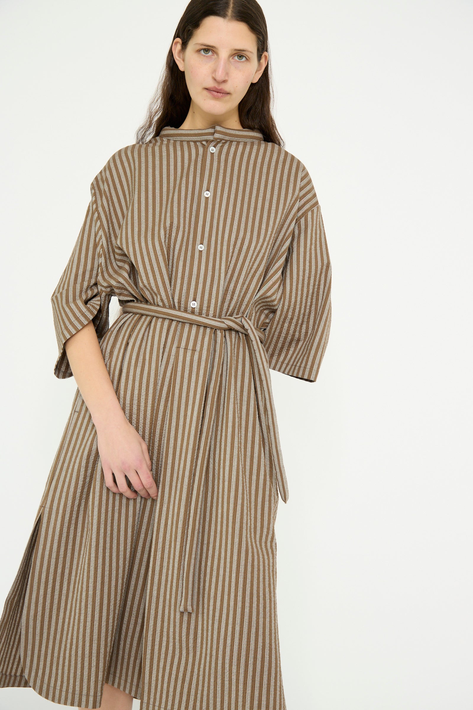 A model stands forward against a white background in a Cristaseya Caftan with Padded Collar in Brown Stripes.