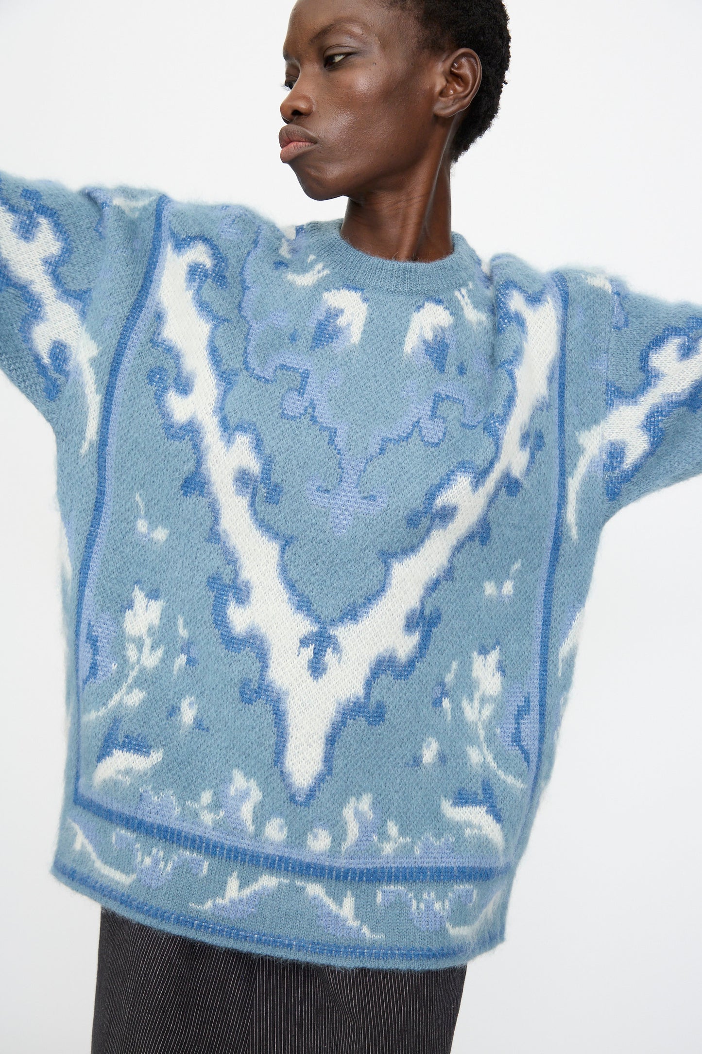 A person wears the Cristaseya Cashmere Oversized Carpet Sweater in Blue and White, crafted from a cashmere wool blend, standing with arms raised against a plain background.