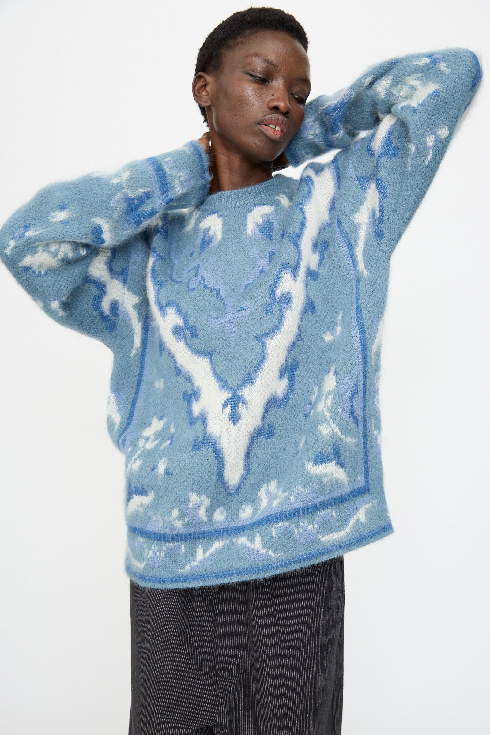 Model wears Cristaseya's Cashmere Oversized Carpet Sweater in Blue and White, crafted from a luxe cashmere wool blend, with dark pants against a plain white background.