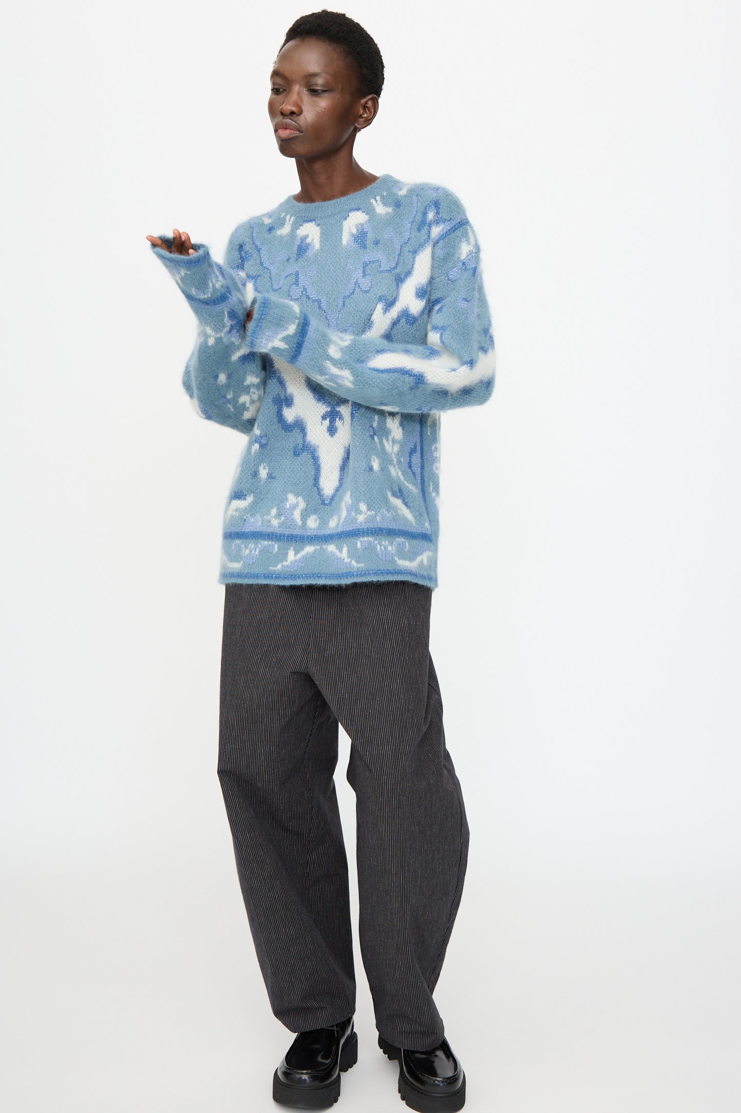 A person wears the Cristaseya Cashmere Oversized Carpet Sweater in Blue and White, paired with dark gray wide-leg pants and black shoes, standing against a plain white background.