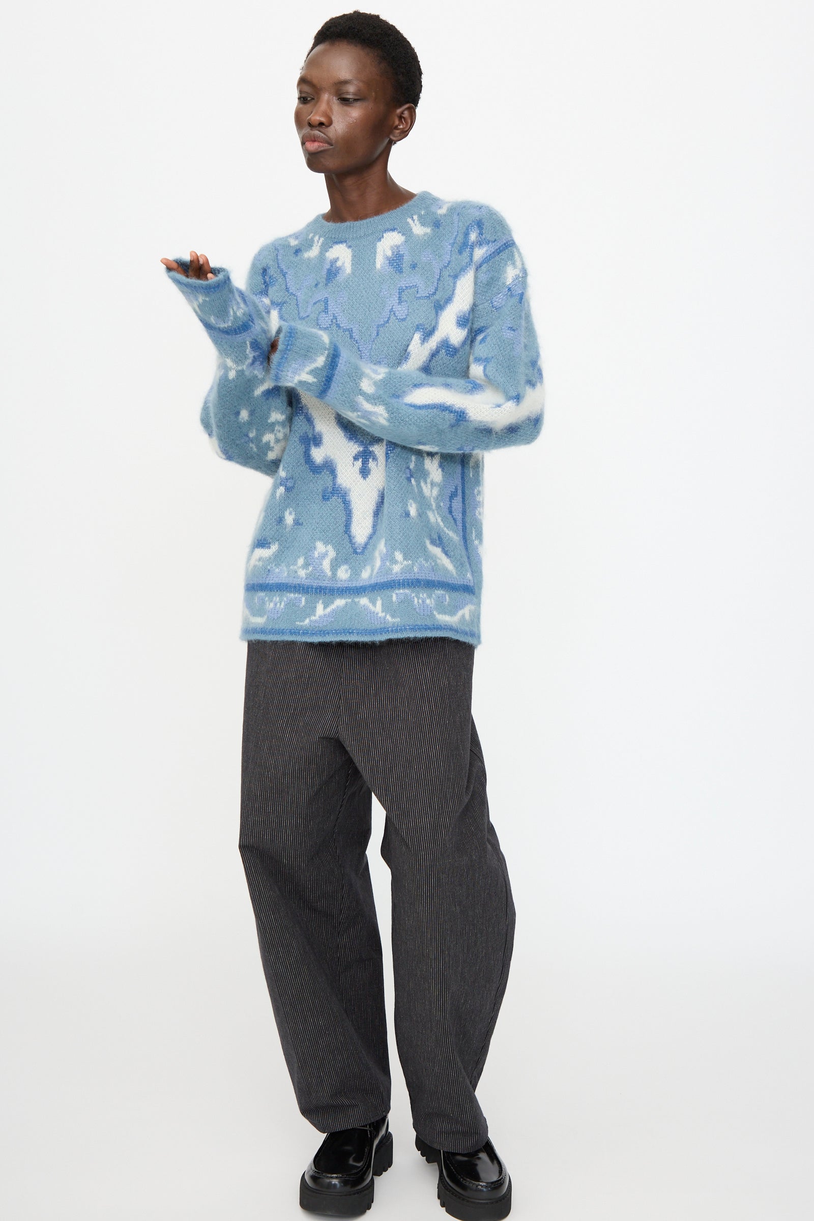 A person wears the Cristaseya Cashmere Oversized Carpet Sweater in Blue and White, paired with dark gray wide-leg pants and black shoes, standing against a plain white background.