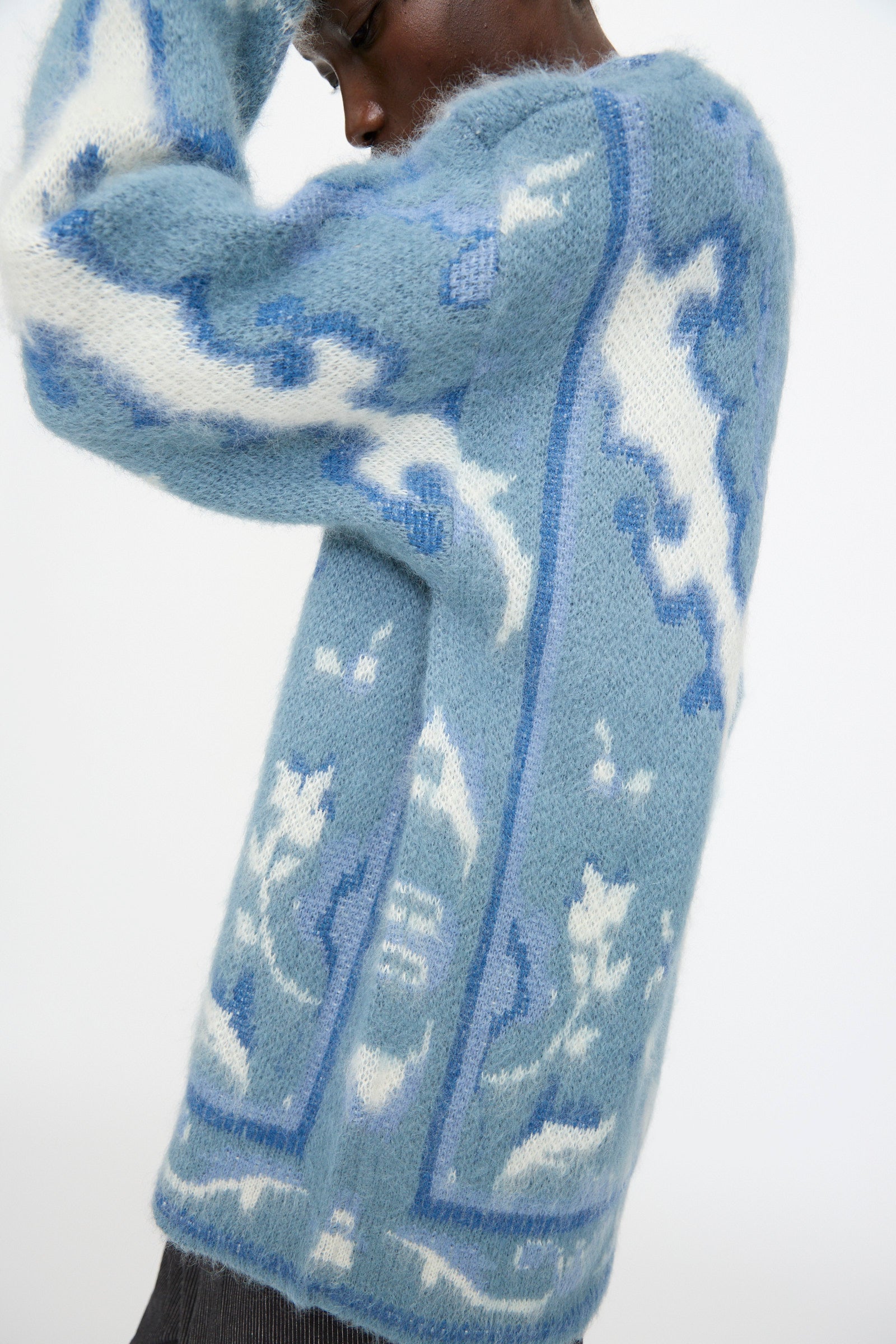 A person wears the Cristaseya Cashmere Oversized Carpet Sweater in Blue and White, featuring a fuzzy wool blend with abstract patterns, standing against a plain background.