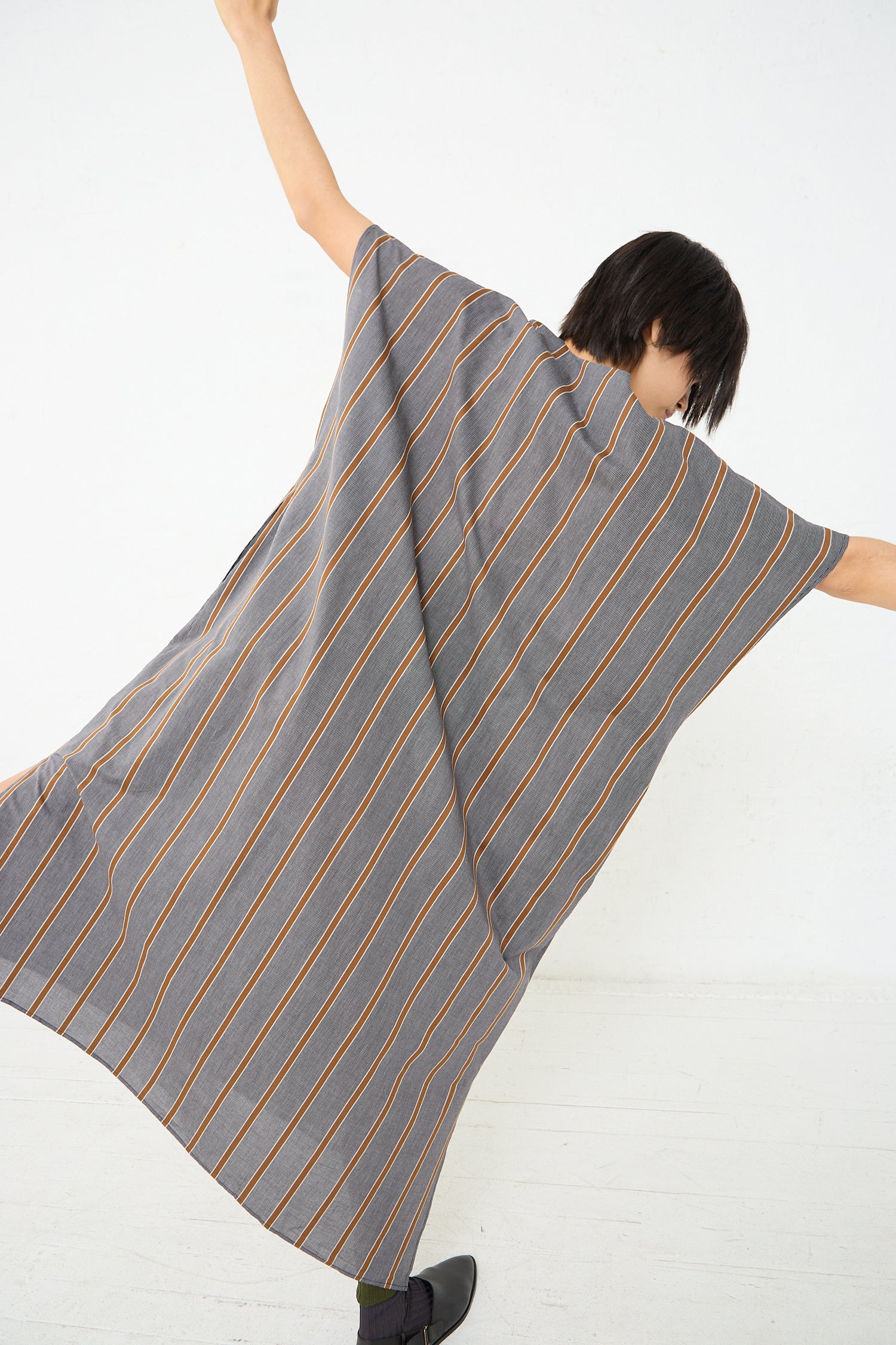 A woman donning an oversized Cristaseya Cotton Caftan in Striped Black and Noisette made from lightweight Japanese cotton with a stylish stripe pattern.