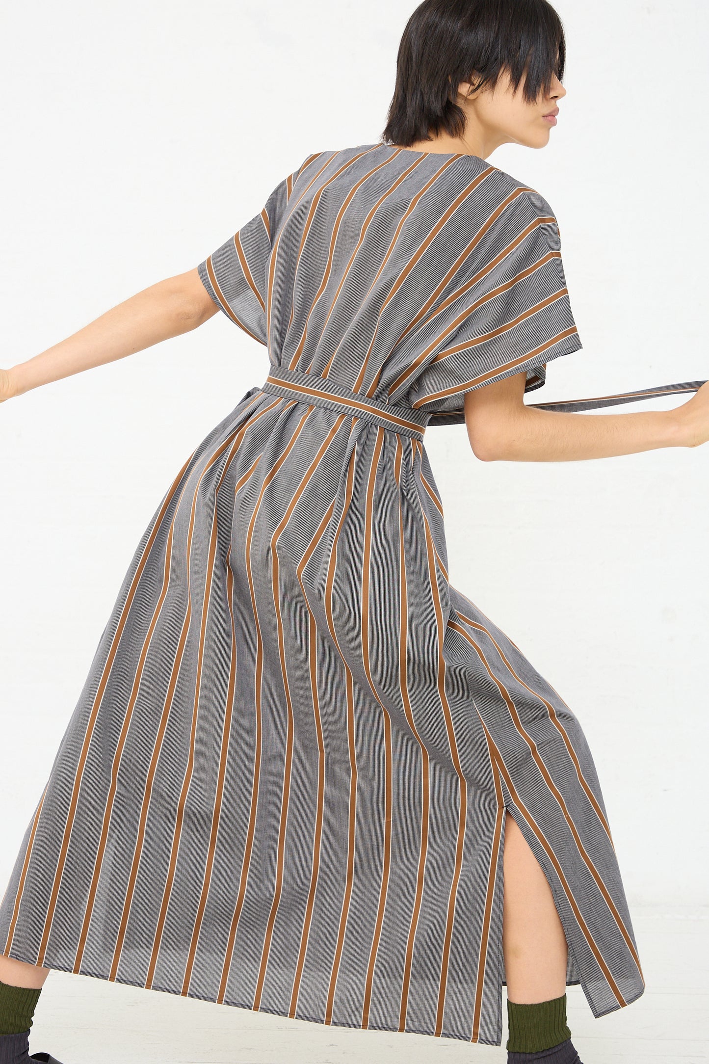 A model wearing an oversized Cristaseya Cotton Caftan in Striped Black and Noisette, made of lightweight Japanese cotton with a stripe pattern. Back view. Model is leaning to the side.