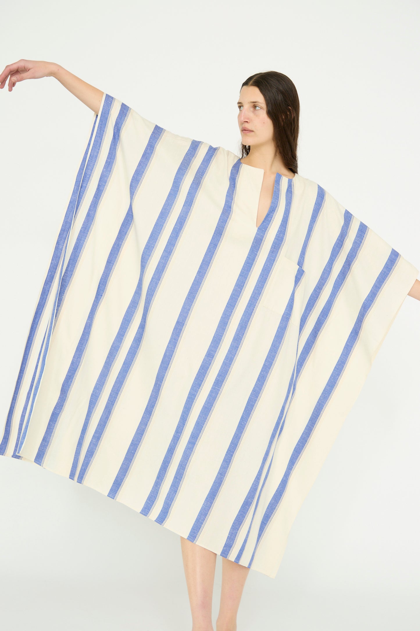 A model is wearing a Cristaseya "Cotton Maxi Caftan in White with Blue Stripes" against a plain background, with arms stretched.