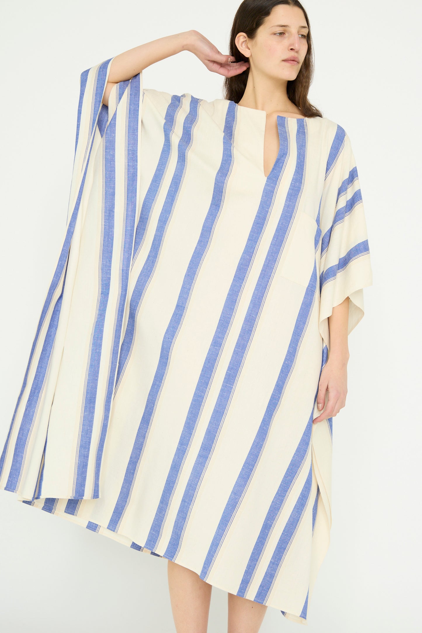 A model poses with one arm raised against a plain background, wearing a Cristaseya Cotton Maxi Caftan in White with Blue Stripes, featuring an oversized fit. 