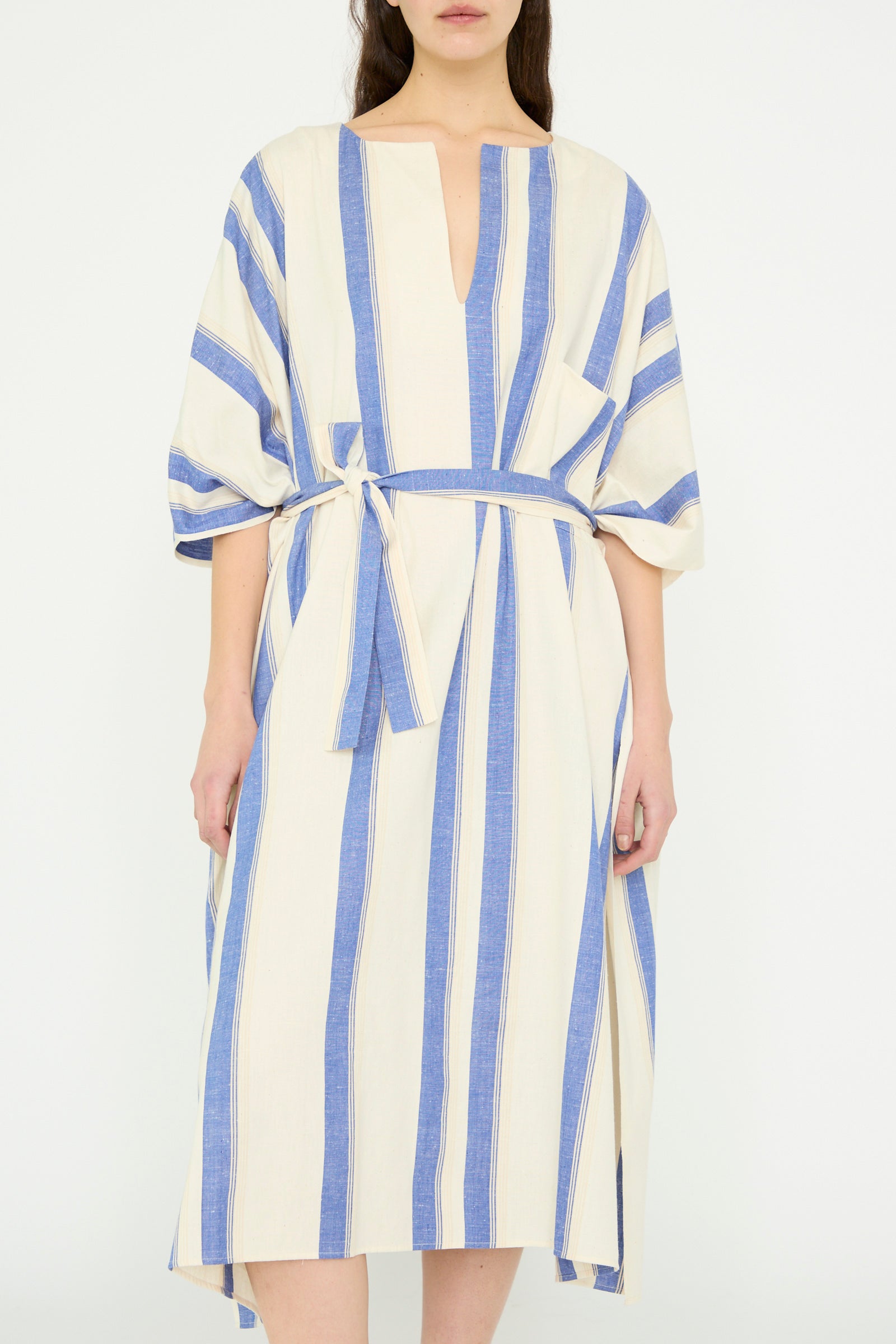 A model is wearing the Cristaseya Cotton Maxi Caftan in White with Blue Stripes, featuring vertical stripes, a V-neck, and waist tie against a white backdrop. 