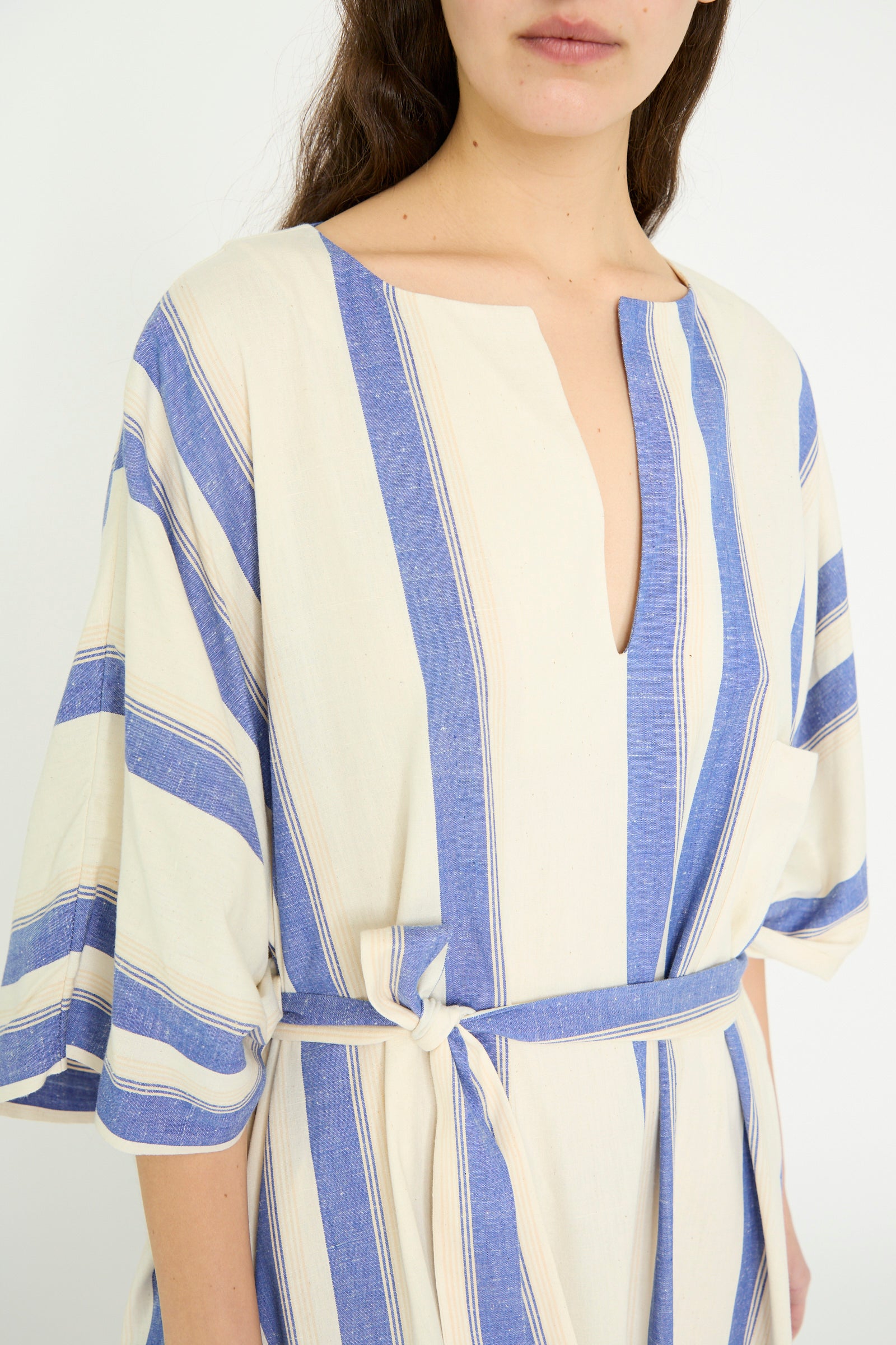 A close-up of a model wearing the Cristaseya Cotton Maxi Caftan in white with blue stripes against a plain backdrop. The dress has wide sleeves, a V-neck, and an oversized fit.