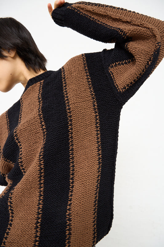 A woman wearing a Cristaseya Fettuccia Striped Sweater in Black and Noisette (Brown) with dropped shoulders.