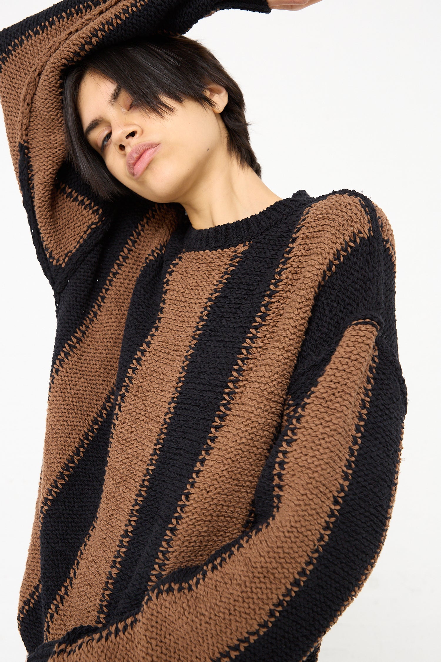 A model wearing a Cristaseya Fettuccia Striped Sweater in Black and Noisette (Brown). Front view.