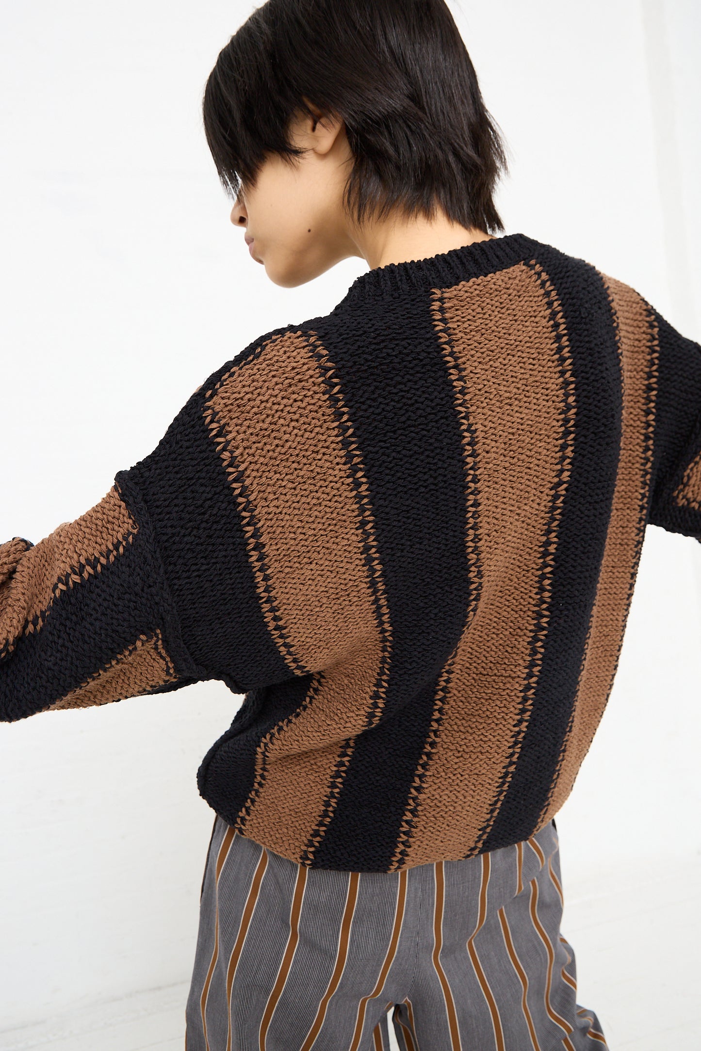 The back of a woman wearing a Cristaseya Fettuccia Striped Sweater in Black and Noisette (Brown) with dropped shoulders.
