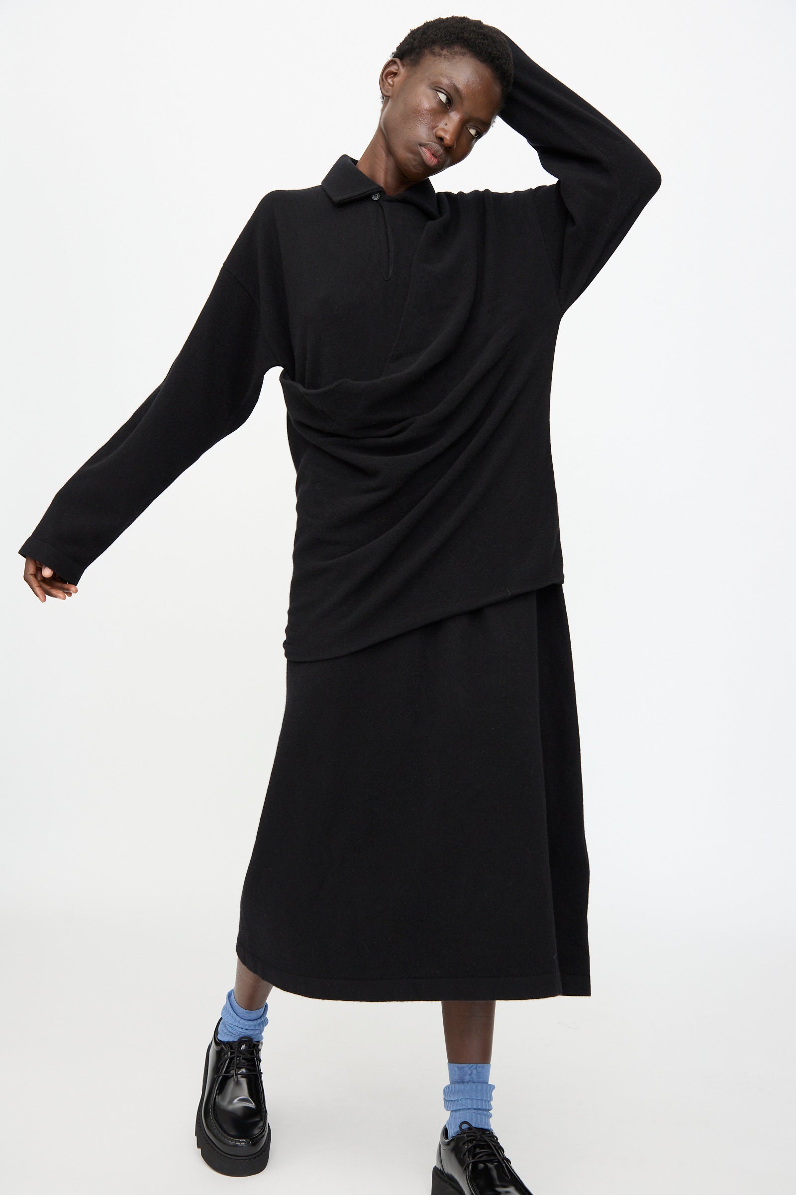 A person stands against a plain white background wearing the Cristaseya Flannel Polo Dress in Black, paired with black shoes and blue socks.