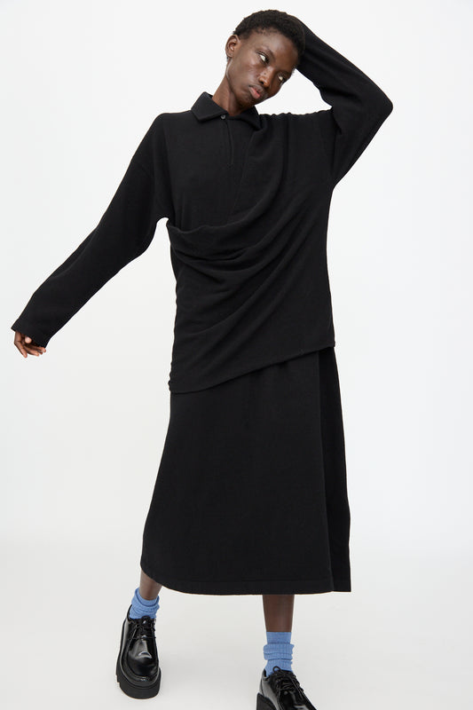 A person stands against a plain white background wearing the Cristaseya Flannel Polo Dress in Black, paired with black shoes and blue socks.