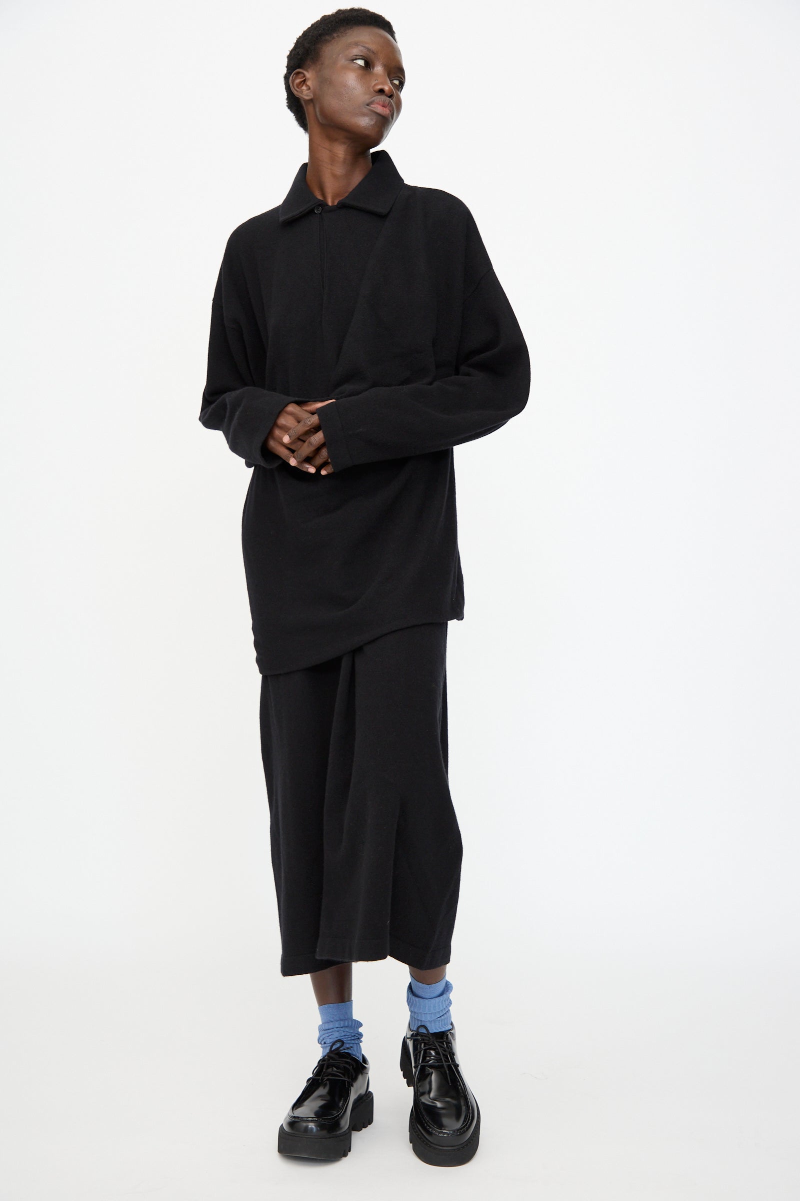 A person stands against a white background, wearing the Cristaseya Flannel Polo Dress in Black, styled with blue socks and black platform shoes.