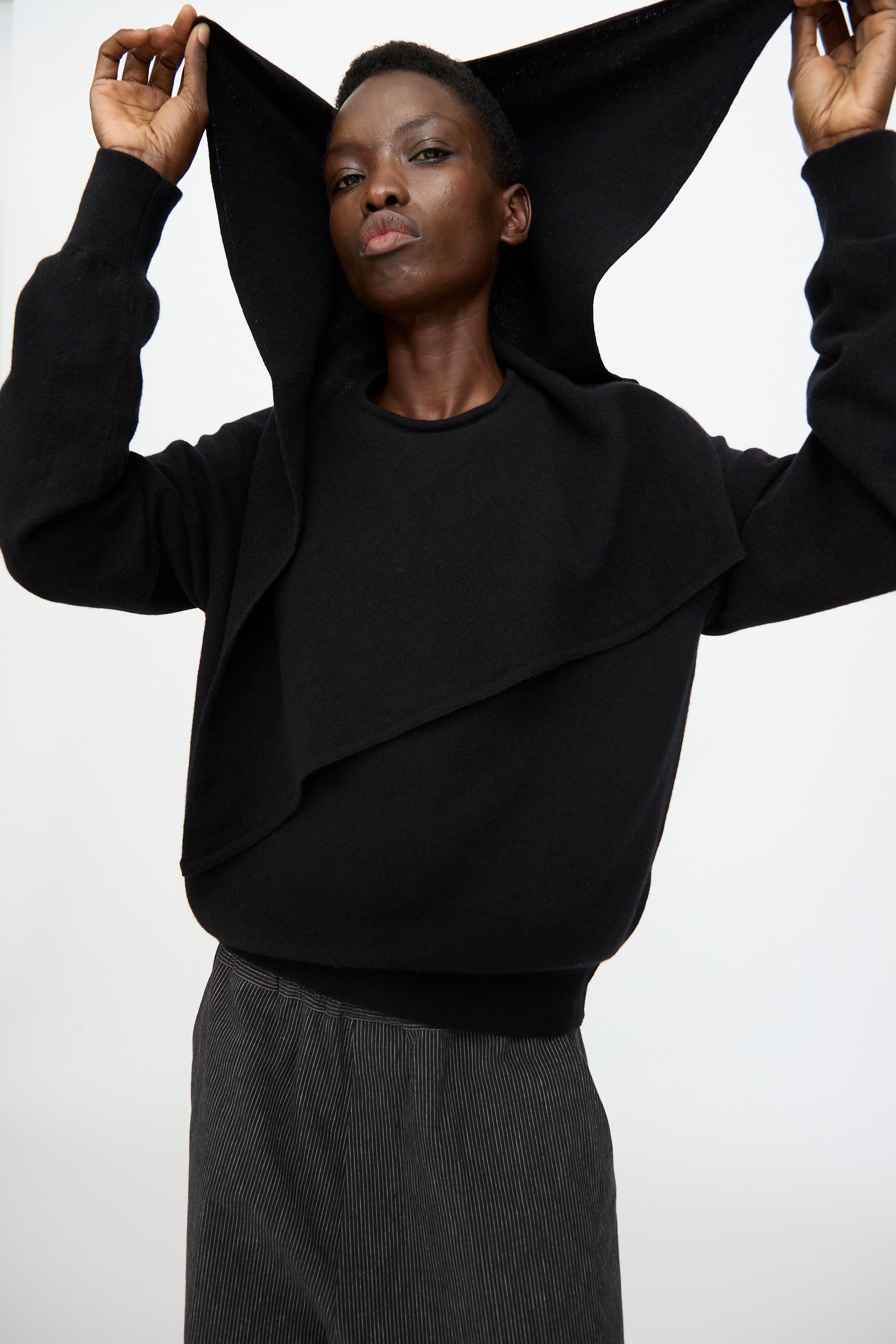 A person wears the Cristaseya Flannel Sailor Collar Sweater in Black, lifting part of the garment over their head while standing against a plain white background.