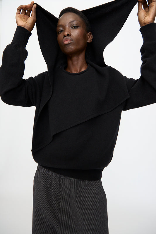A person wears the Cristaseya Flannel Sailor Collar Sweater in Black, lifting part of the garment over their head while standing against a plain white background.