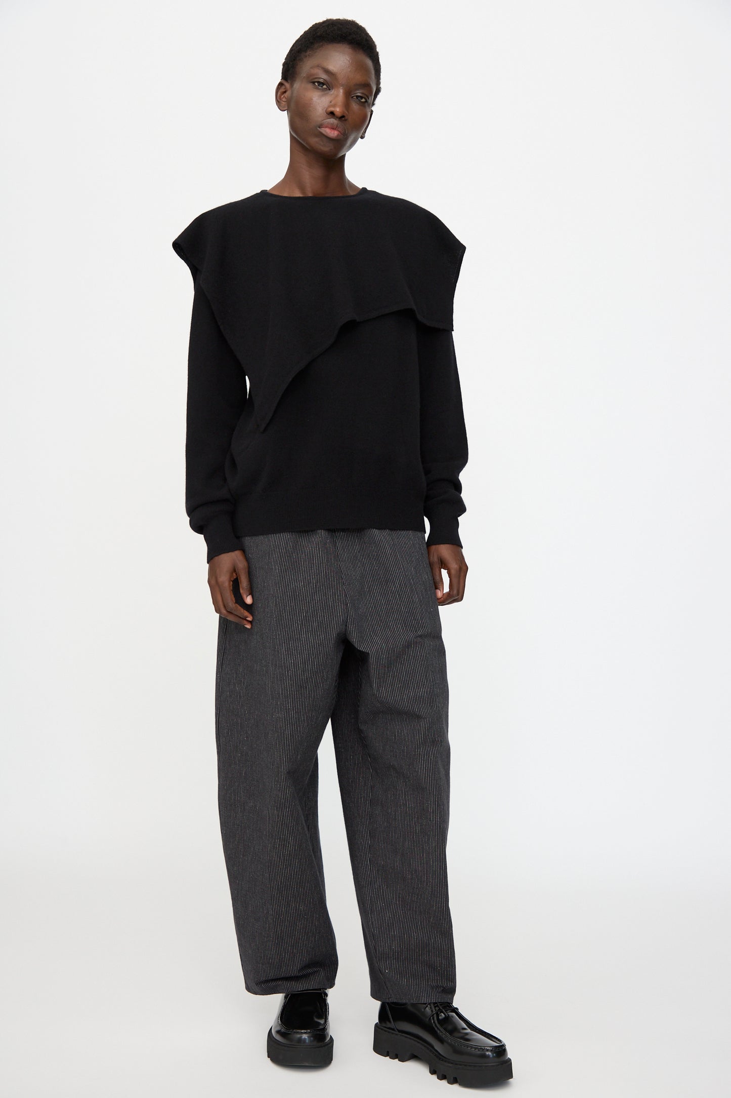Person standing against a plain background, wearing Cristaseya's Flannel Sailor Collar Sweater in Black, wide-leg gray pinstripe pants, and black chunky shoes.