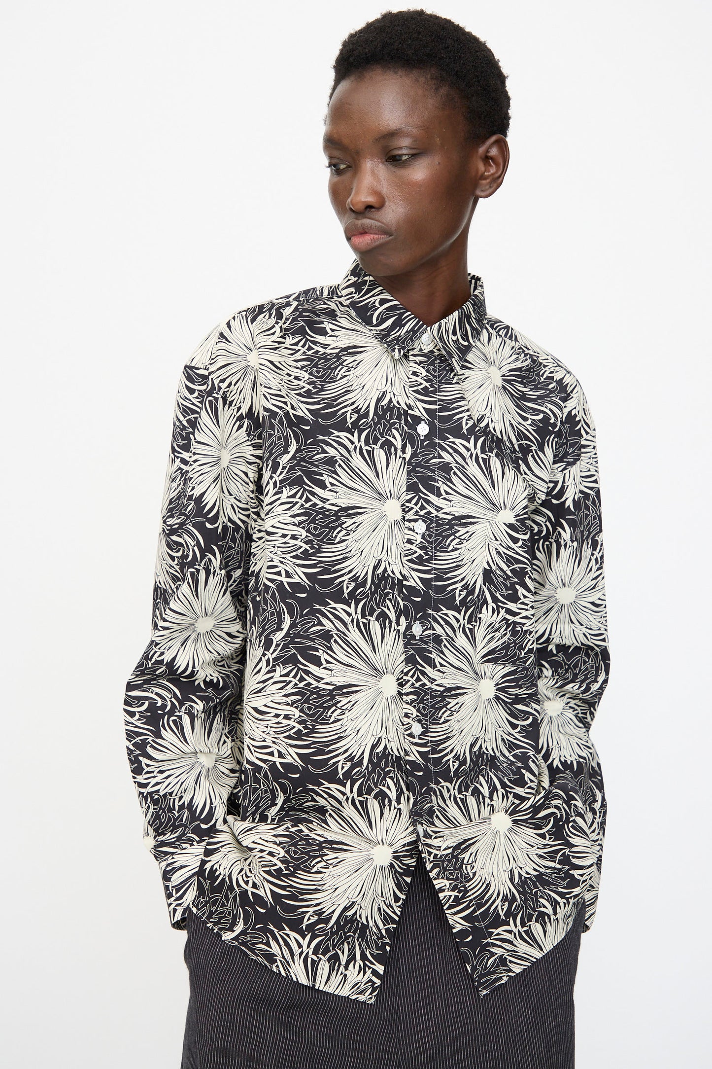 A person wears the Cristaseya Handmade Classic Collar Shirt in Black with White Flowers, paired with dark striped pants, standing against a plain light background.