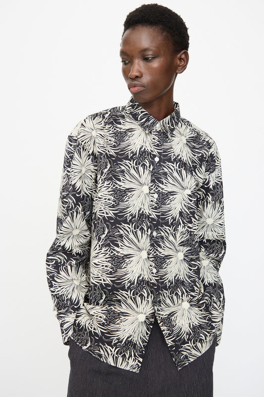 A person wears the Cristaseya Handmade Classic Collar Shirt in Black with White Flowers, paired with dark striped pants, standing against a plain light background.