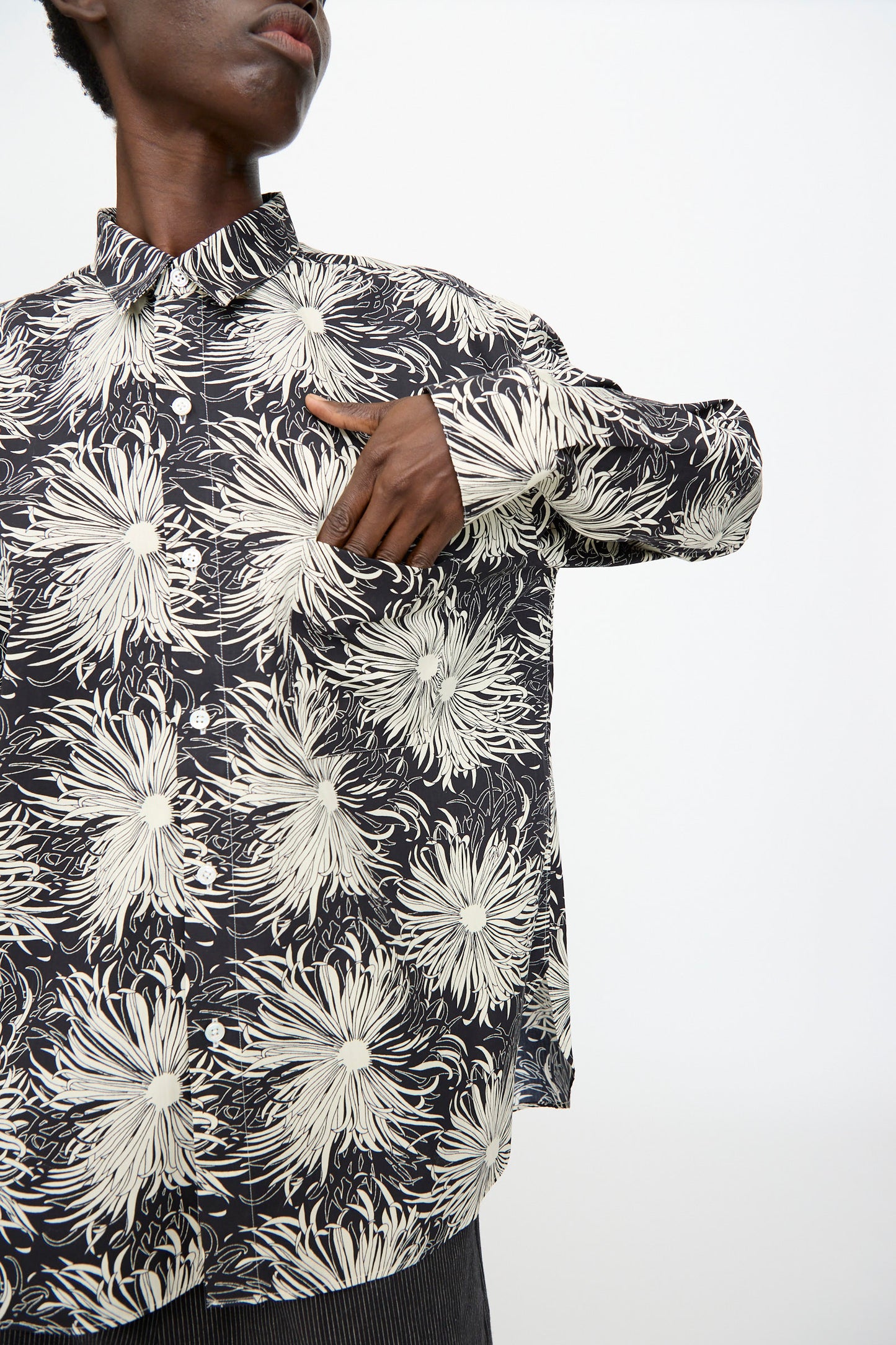 A person points to the pocket of the Cristaseya Handmade Classic Collar Shirt in Black with White Flowers, standing against a plain background.