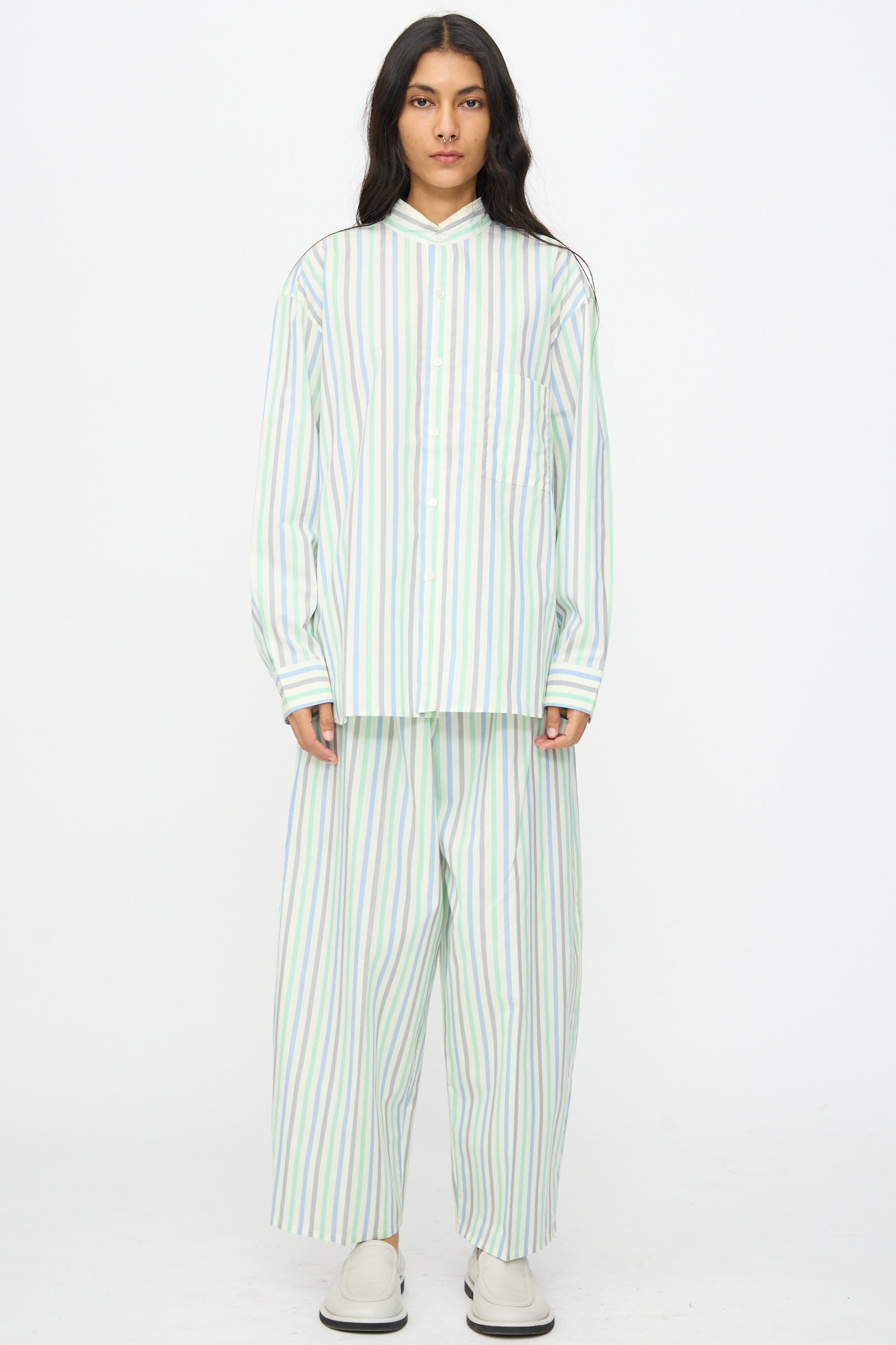 A person stands against a white background wearing the Cristaseya Handmade Fringed Mao Collar Shirt in Striped Pastel Green, paired with matching wide-leg pants and white slip-on shoes.