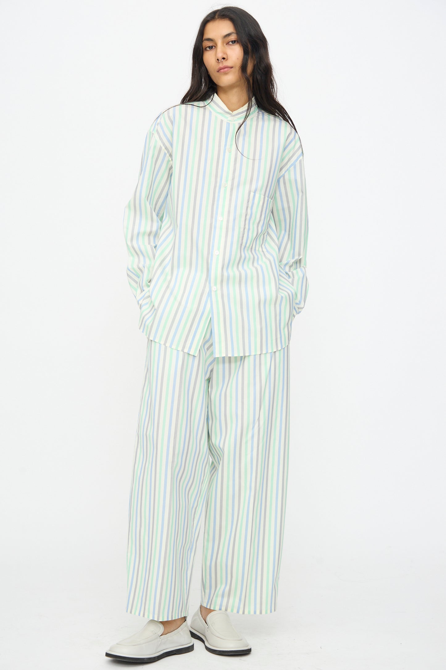 A person stands against a white background wearing the Cristaseya Handmade Fringed Mao Collar Shirt in Striped Pastel Green, styled with matching wide-leg pants and white slip-on shoes.