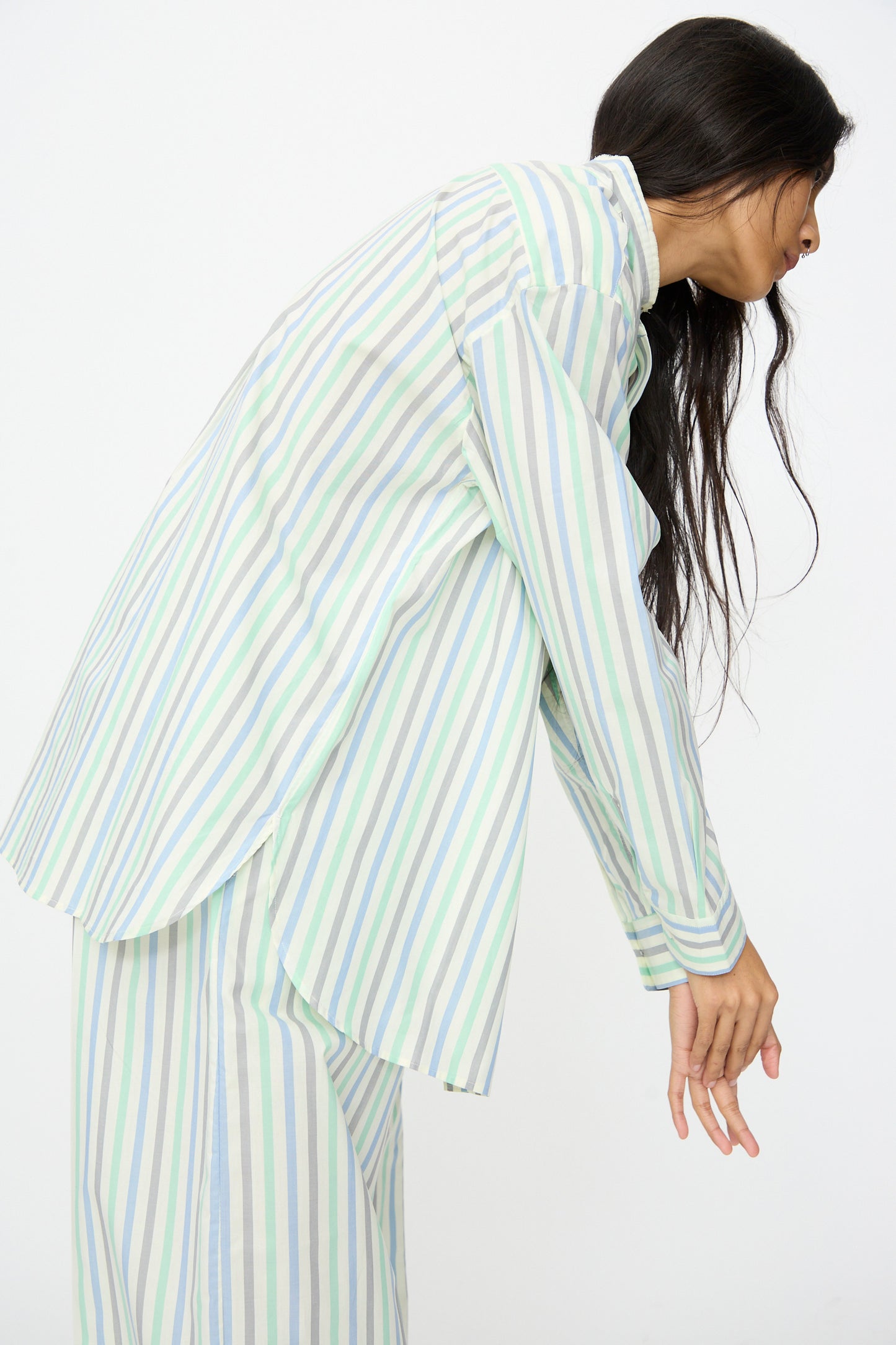 A person wears the Cristaseya Handmade Fringed Mao Collar Shirt in Striped Pastel Green, leaning forward with arms relaxed against a plain white background.
