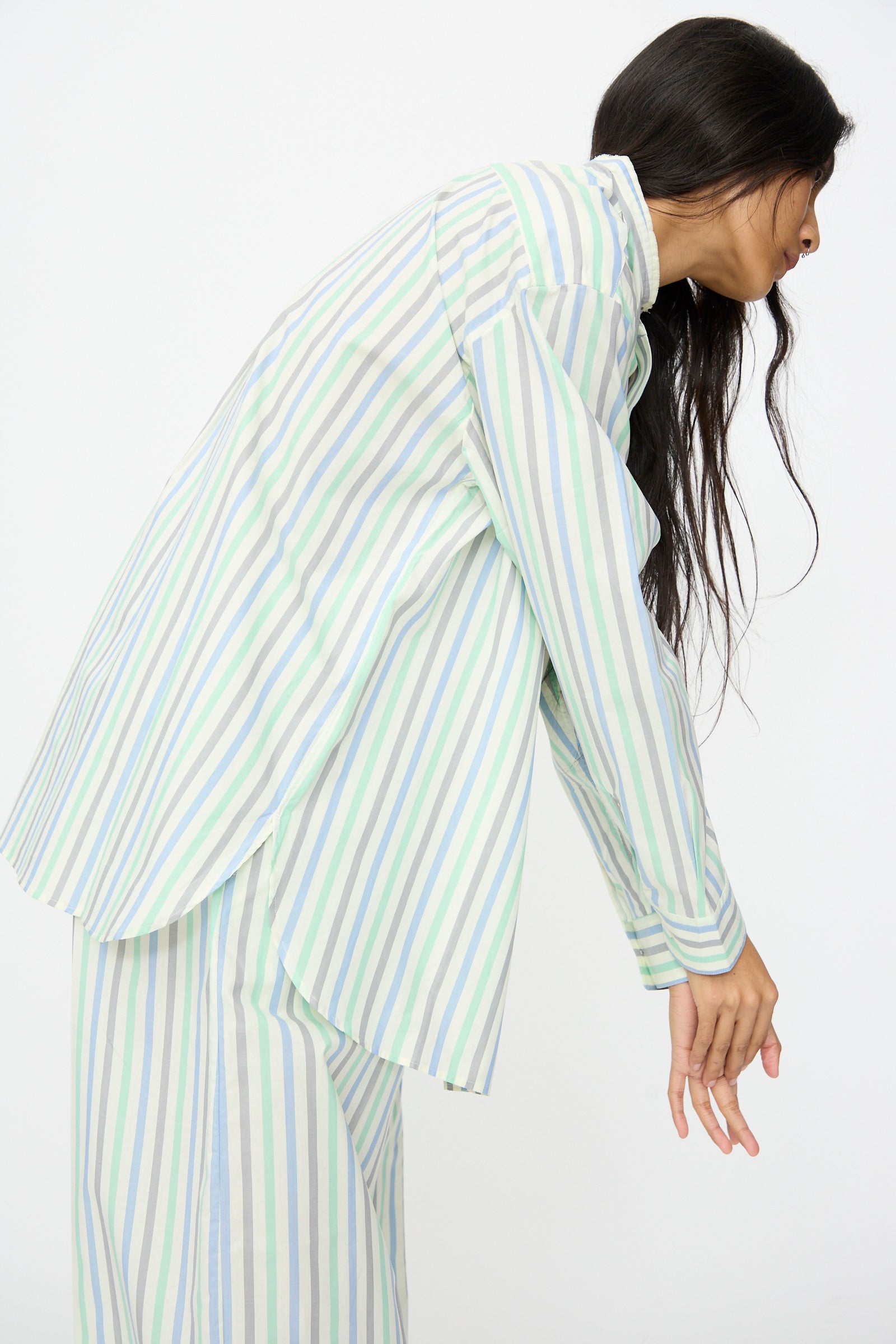 A person wears the Cristaseya Handmade Fringed Mao Collar Shirt in Striped Pastel Green, leaning forward with arms relaxed against a plain white background.