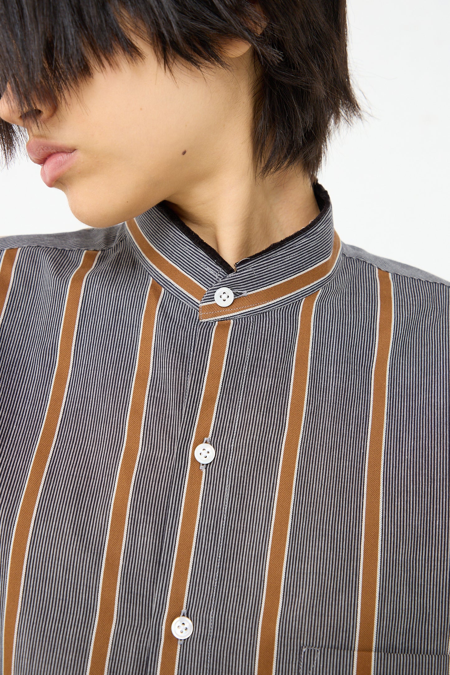 An up close view of a woman wearing a Cristaseya Mao Shirt with Fringed Collar in Striped Black and Noisette.
