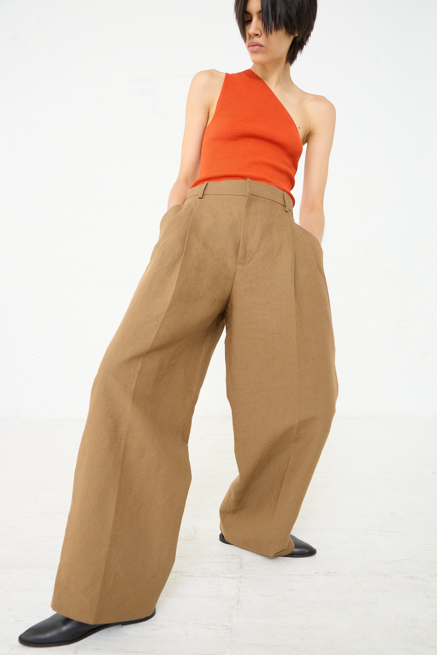 A woman in a Cristaseya Japanese Washi and Linen Canvas Double Pleated Wide Trouser in Mocha and wearing a red top.
