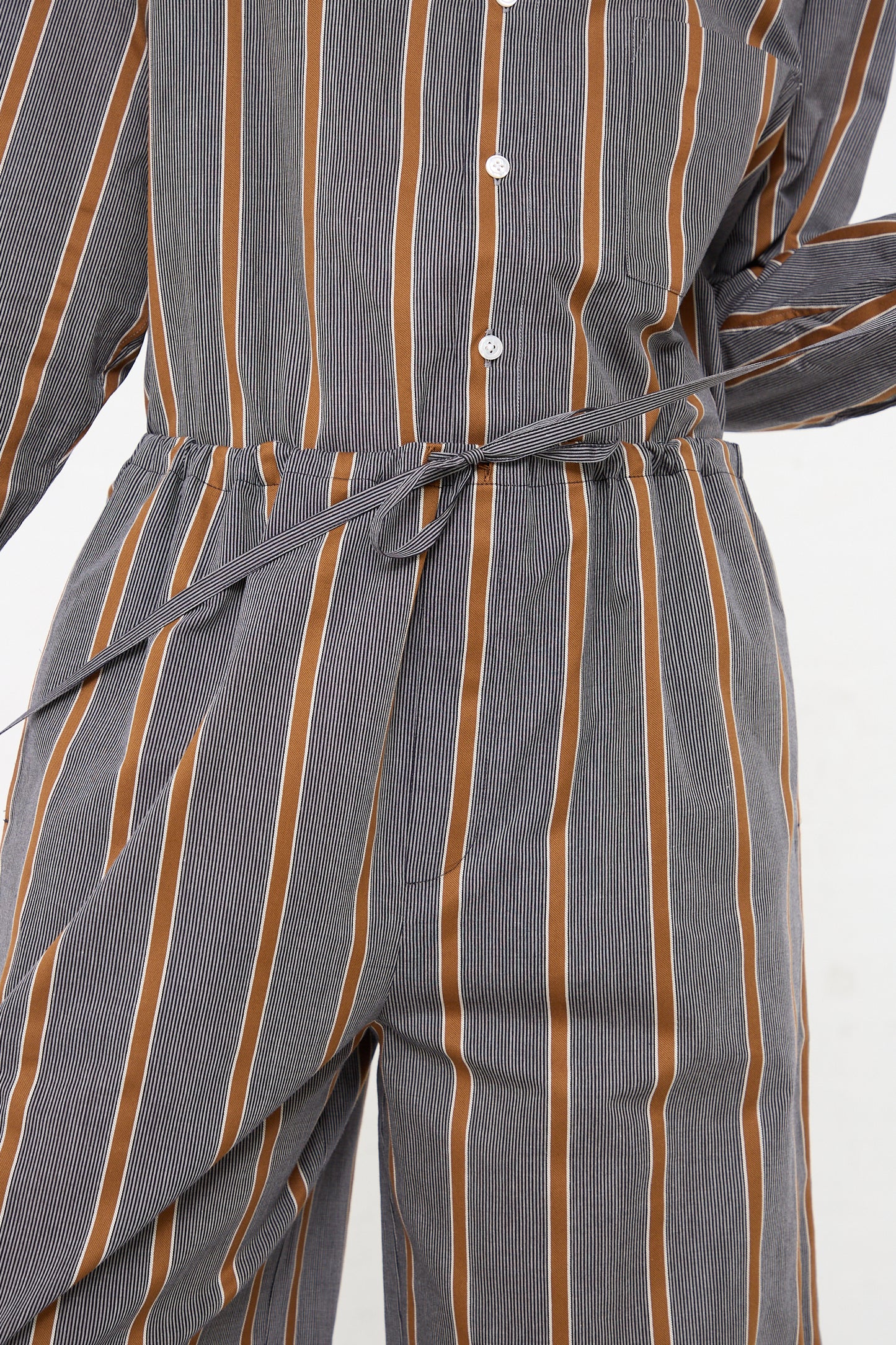 A woman wearing the Cristaseya Maxi Large Pant in Striped Black and Noisette, a lightweight Japanese cotton jumpsuit with wide leg and an oversized drawstring pant in grey and orange stripes.