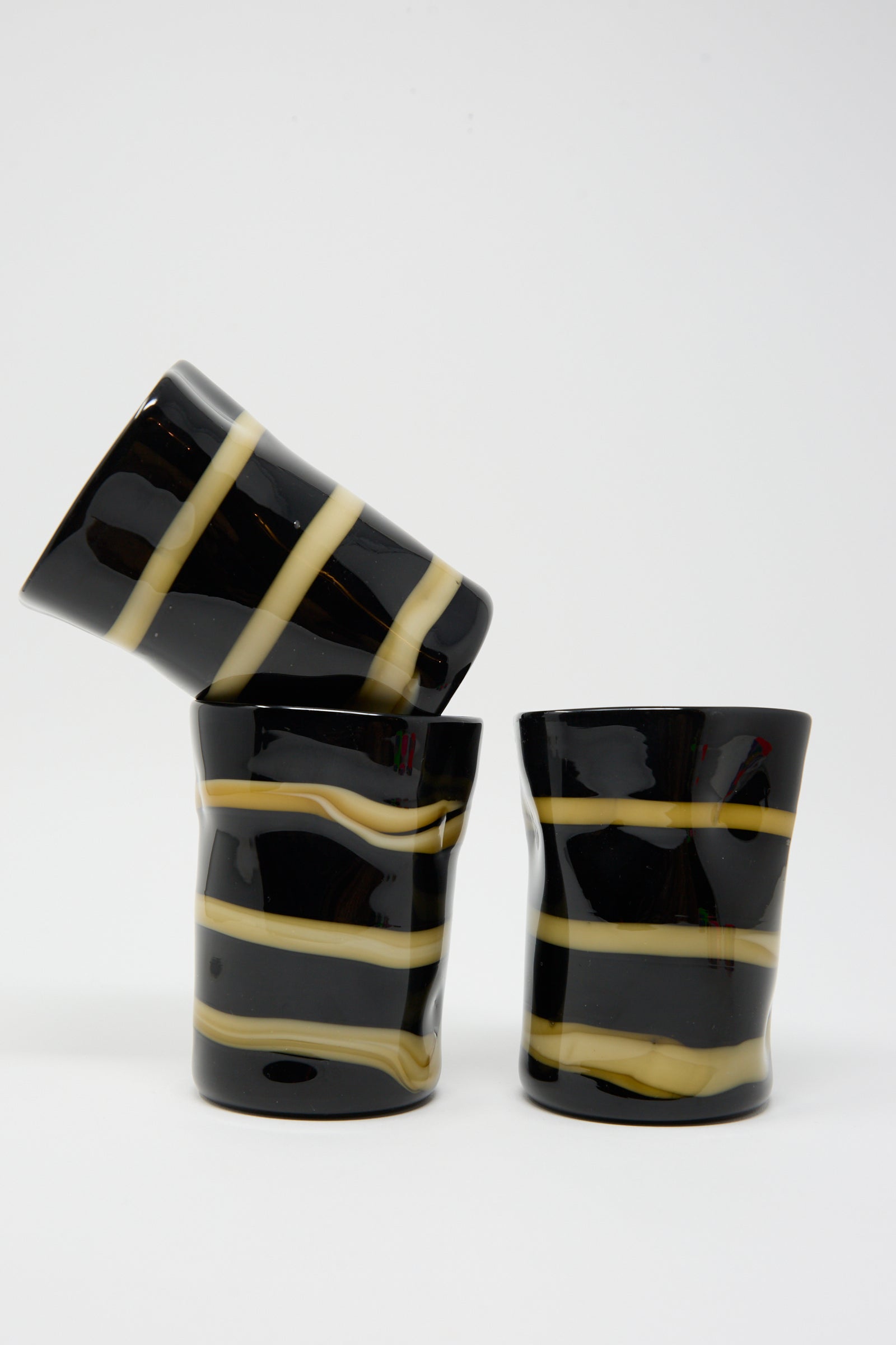 Three Murano Glass pieces in Black with Ocher Stripes by Cristaseya. One glass is leaning diagonally over the other two, set against a plain white background.