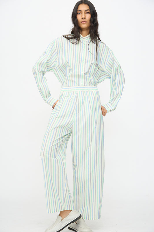 A person stands against a white background, wearing Cristaseya Oversized Pyjama Pants in Striped Pastel Green styled with a matching loose shirt and white shoes.