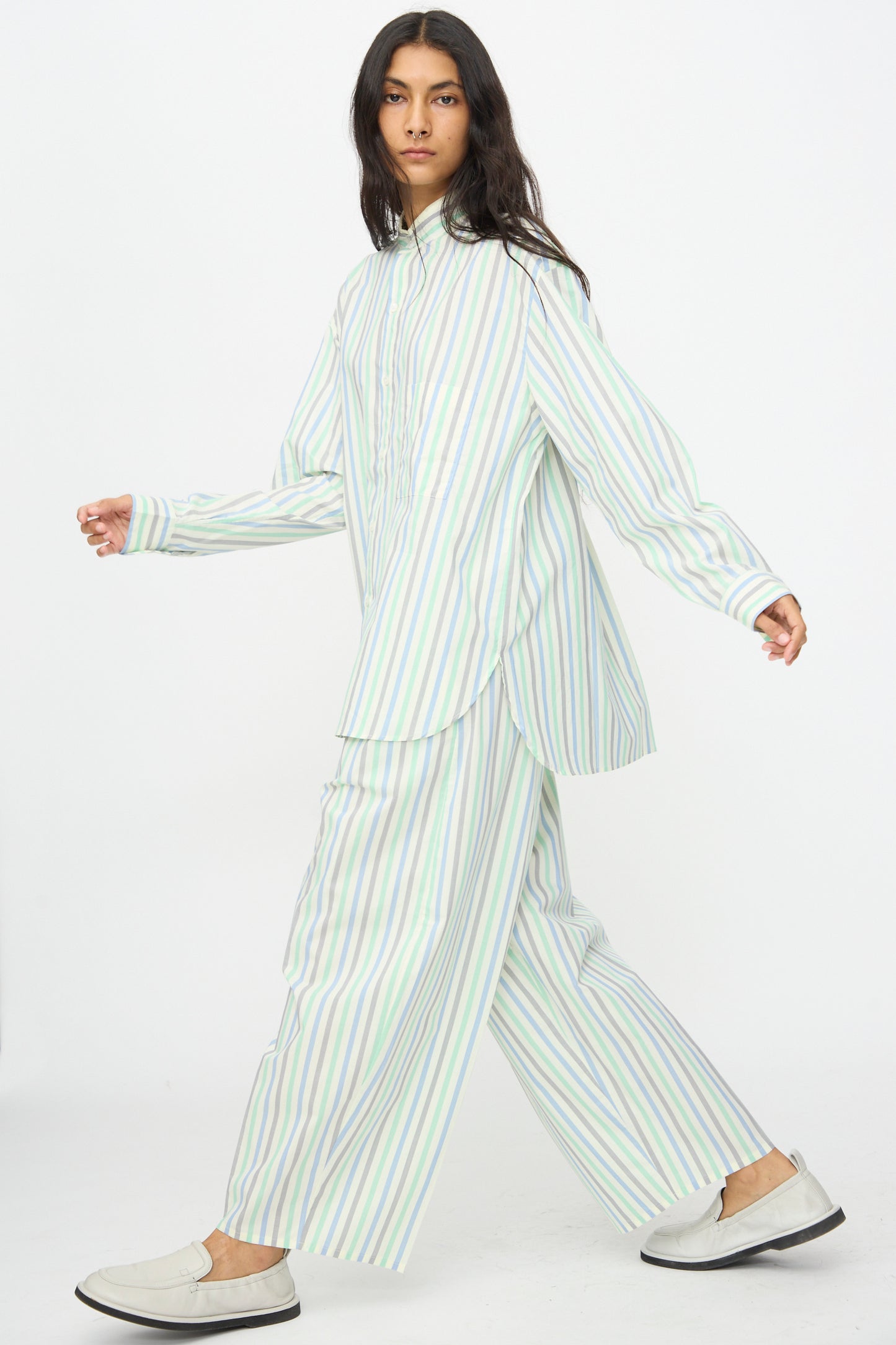 A person wears Cristaseya's Oversized Pyjama Pants in Striped Pastel Green, paired with a loose button-up shirt and light slip-on shoes, walking against a plain white background.