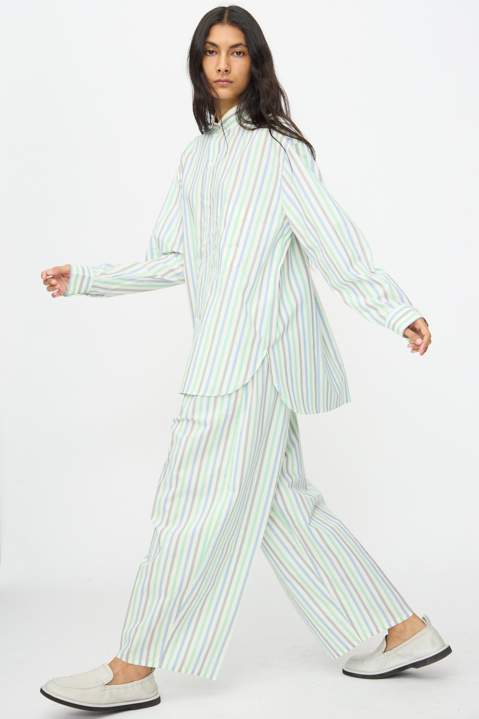 A person wears Cristaseya's Oversized Pyjama Pants in Striped Pastel Green, paired with a loose button-up shirt and light slip-on shoes, walking against a plain white background.