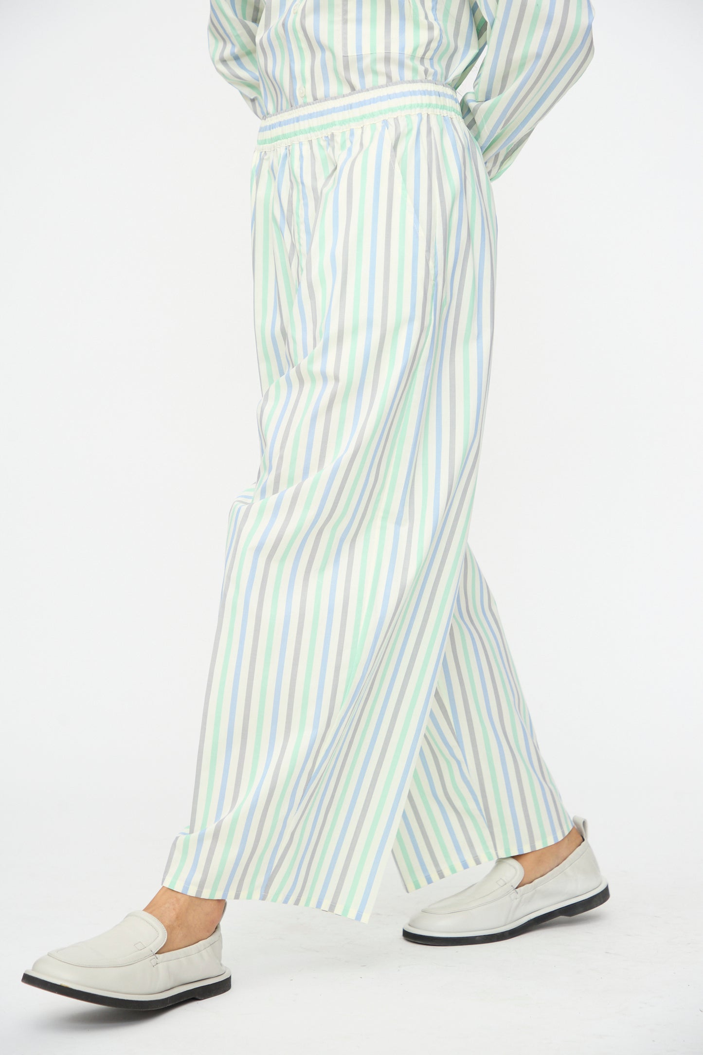 A person wears Cristaseya’s Oversized Pyjama Pants in Striped Pastel Green with white loafers, photographed against a plain white background.