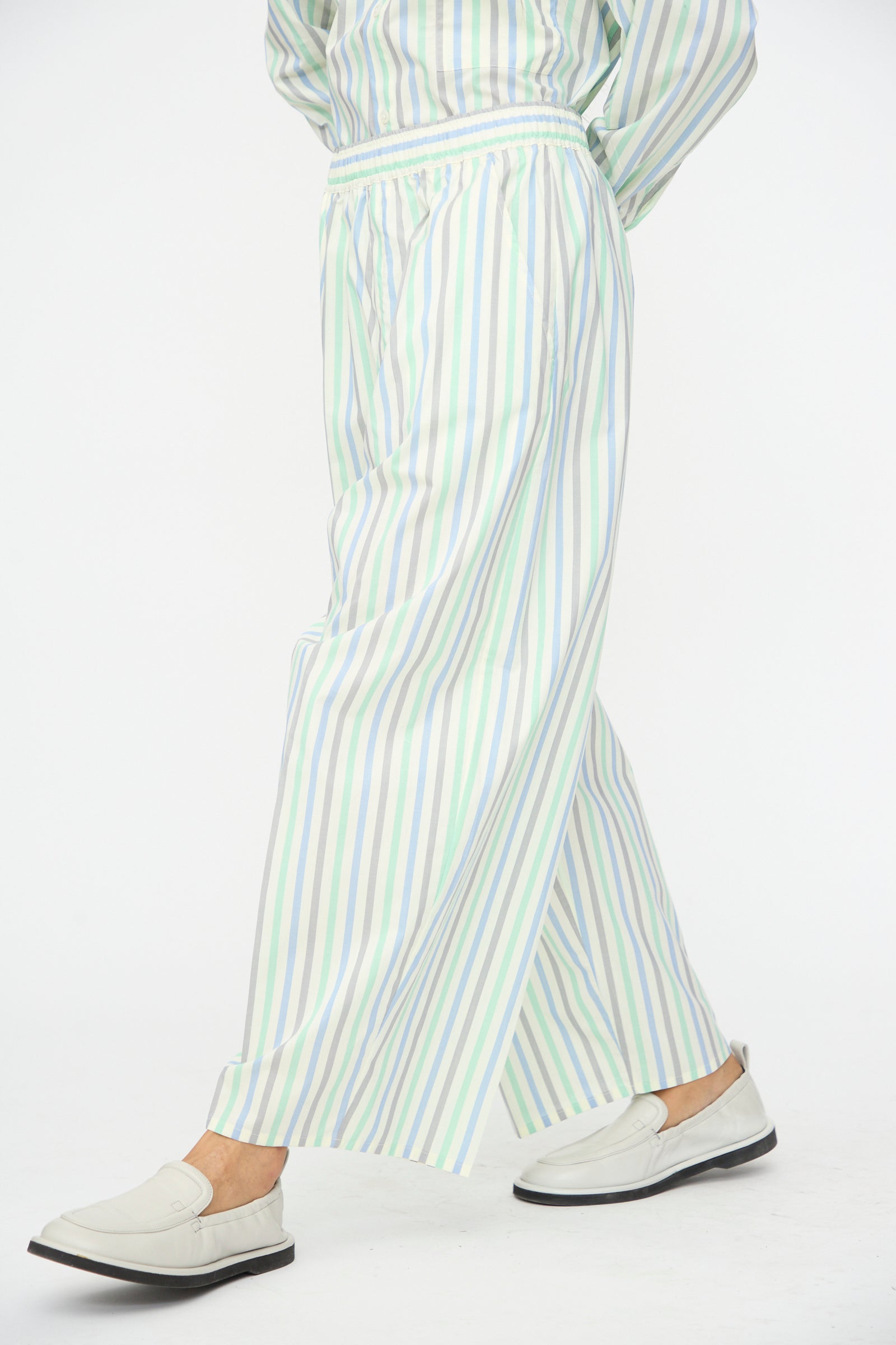 A person wears Cristaseya’s Oversized Pyjama Pants in Striped Pastel Green with white loafers, photographed against a plain white background.
