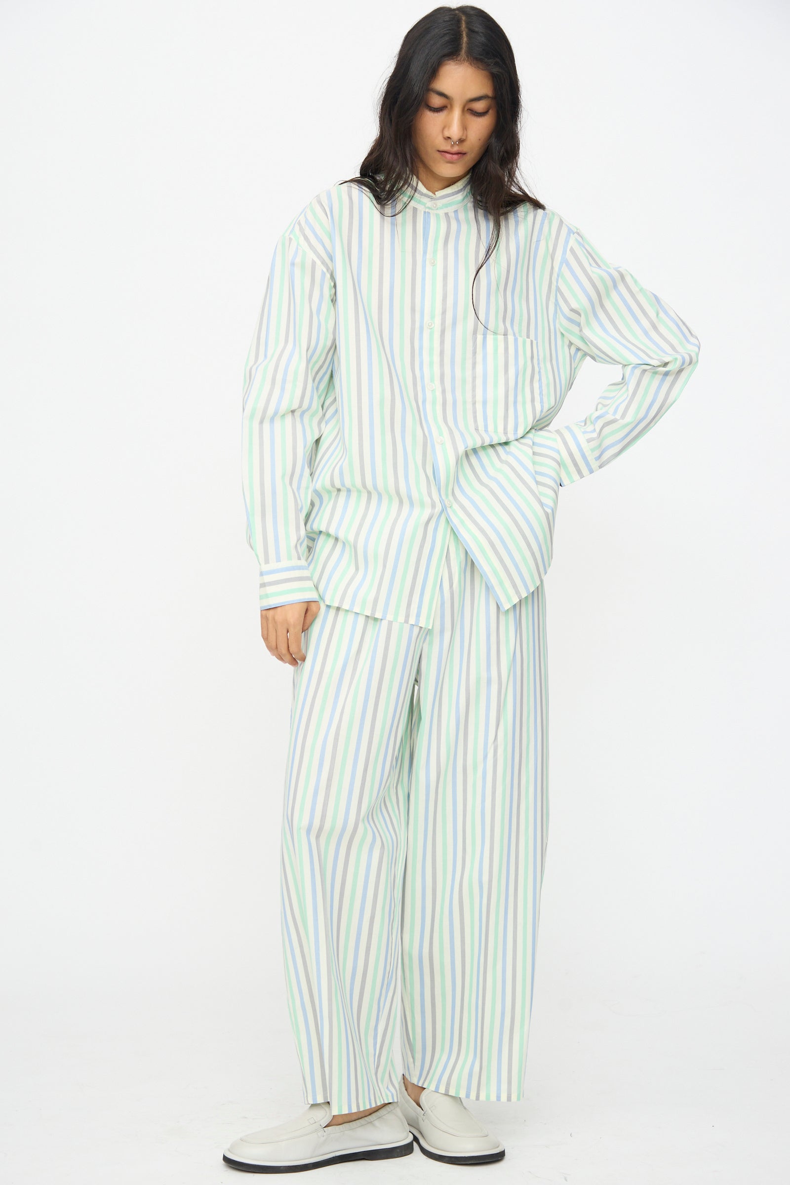 A person stands against a white background in a loose shirt, Cristaseya Oversized Pyjama Pants in Striped Pastel Green, and white shoes.