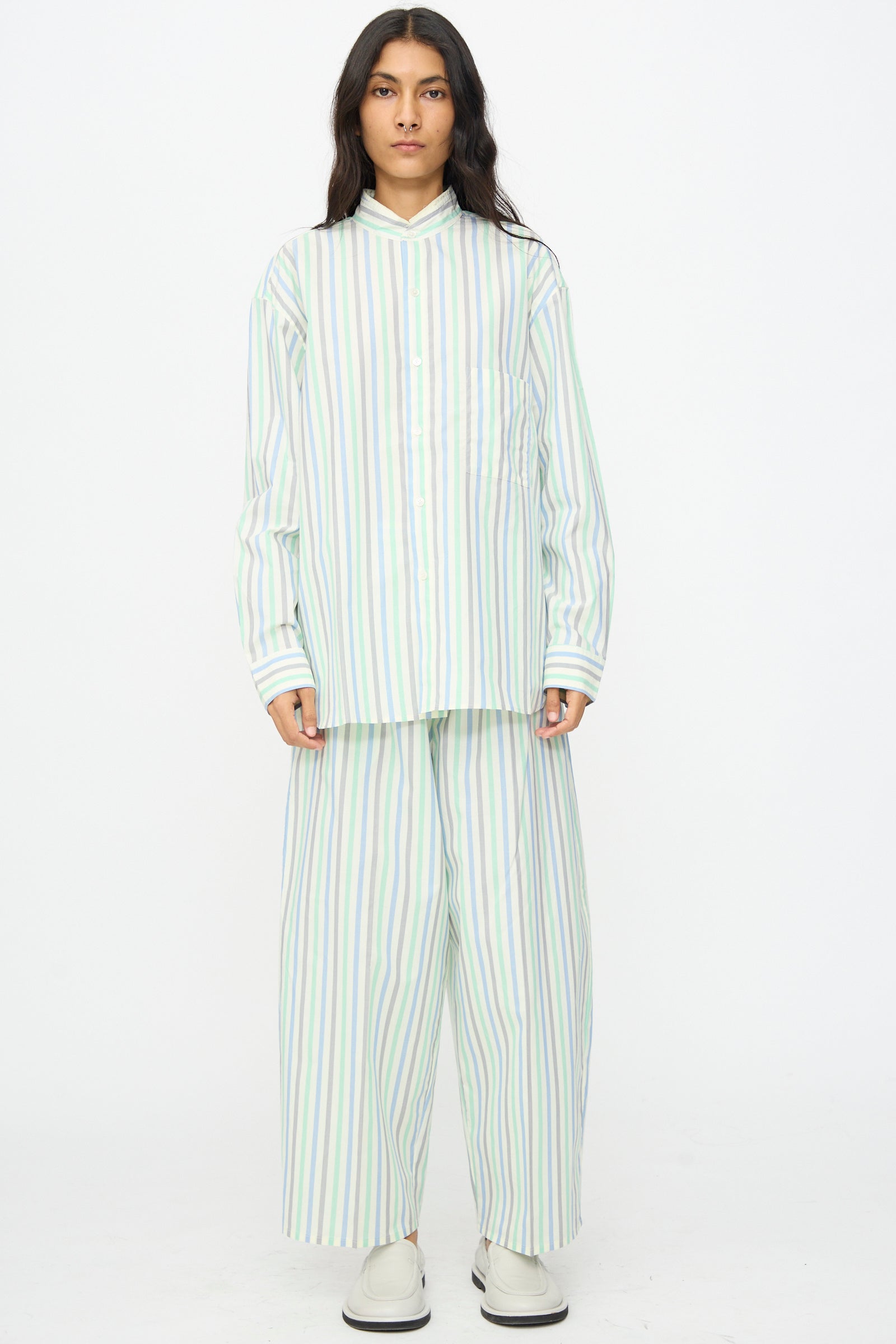 A person wearing Cristaseya Oversized Pyjama Pants in Striped Pastel Green stands against a plain white background, paired with a loose-fitting, long-sleeve, button-up shirt.