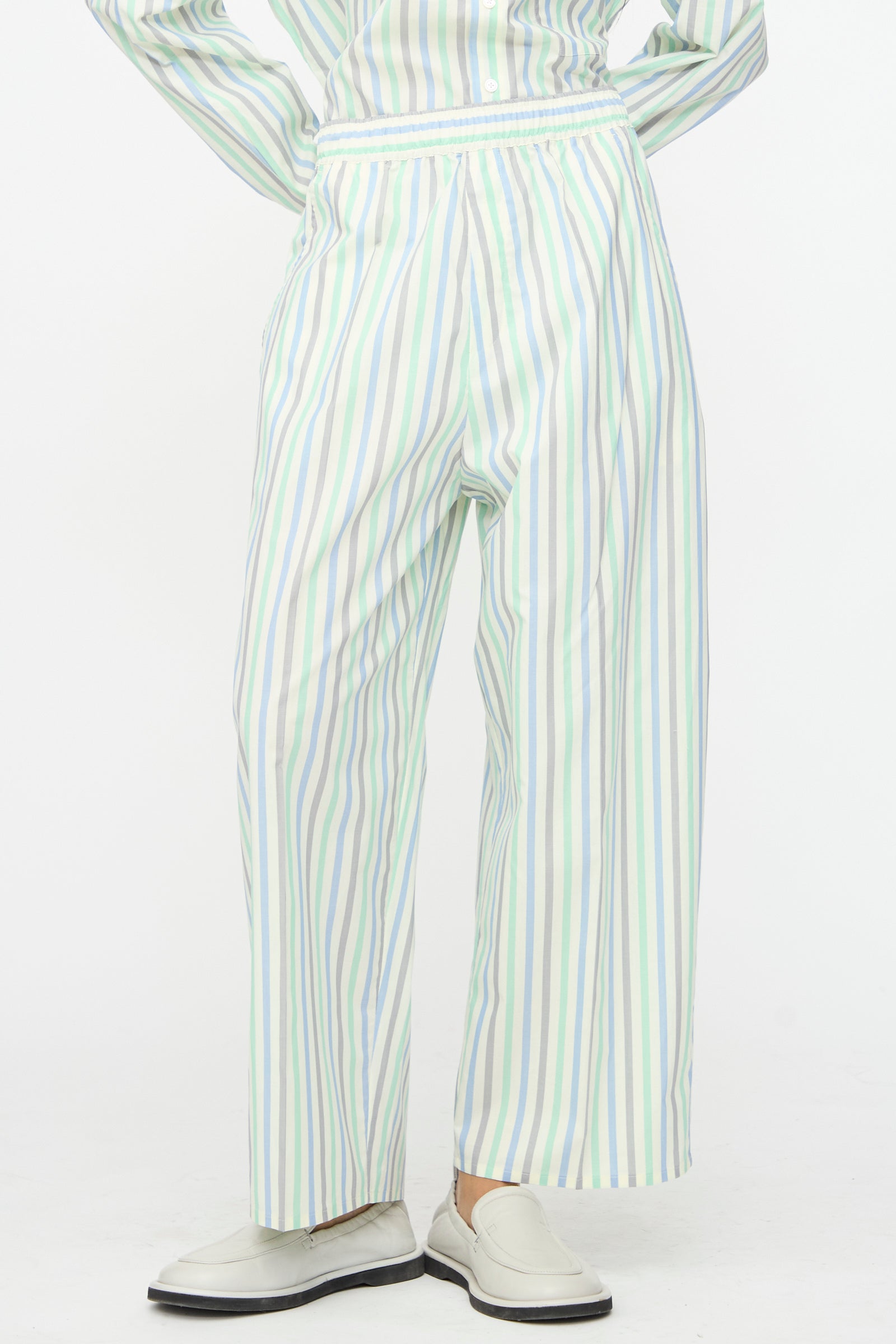 A person wears Cristaseya's Oversized Pyjama Pants in Striped Pastel Green with white loafers, standing against a plain white background.