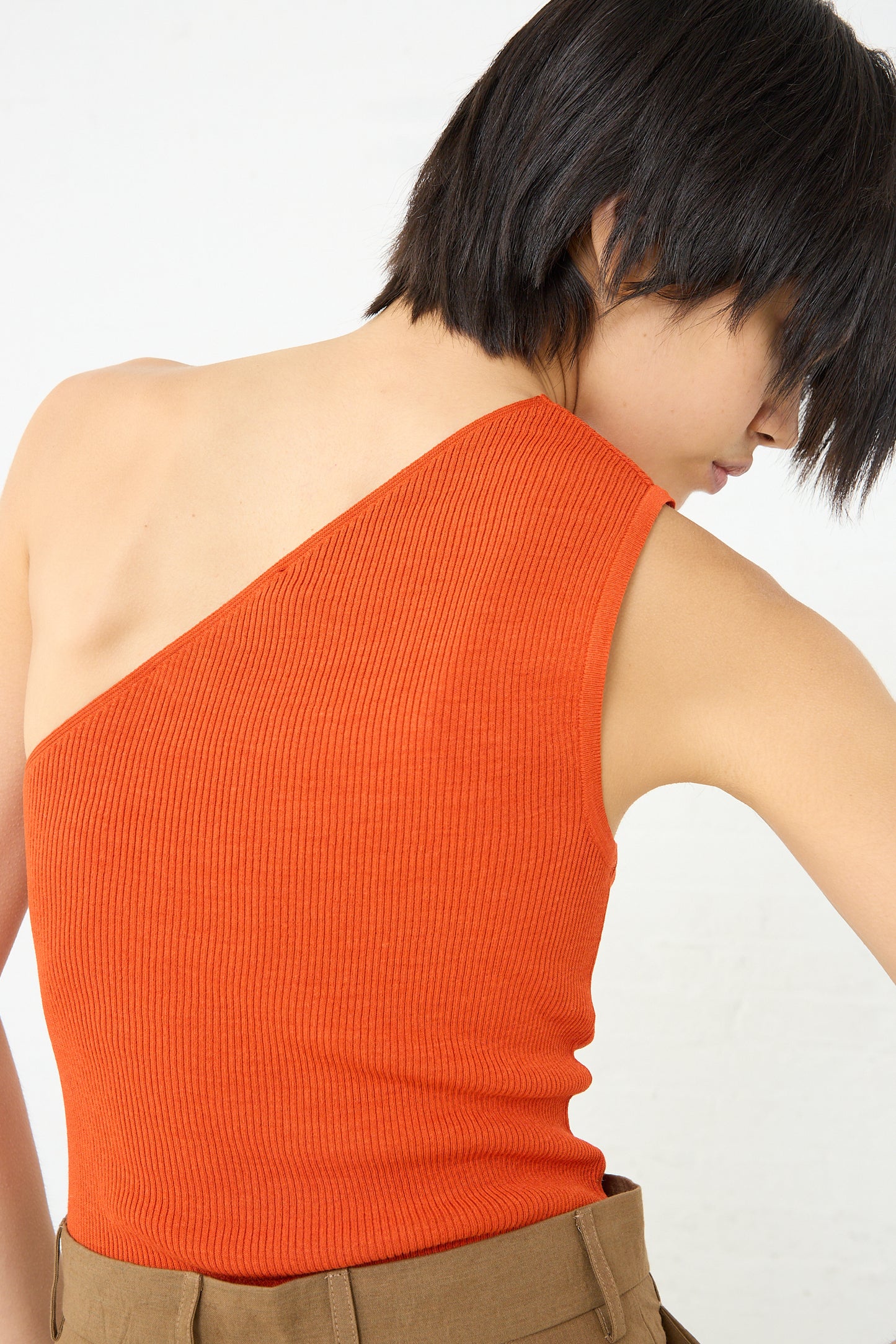 The back of a woman wearing a Cristaseya Ribbed Silk Asymmetrical Top in Orange.
