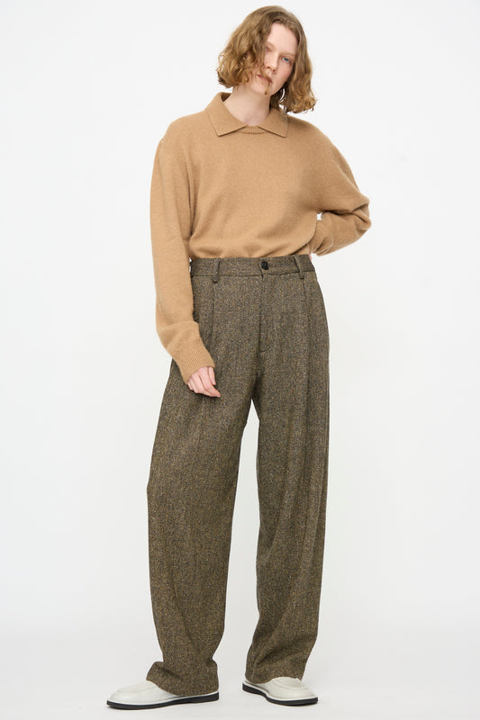 A person wearing a tan long-sleeve sweater, the Cristaseya Tweed Double Pleated Wide Pants in Brown and Black, and white sneakers stands against a plain white background with one hand on their hip.