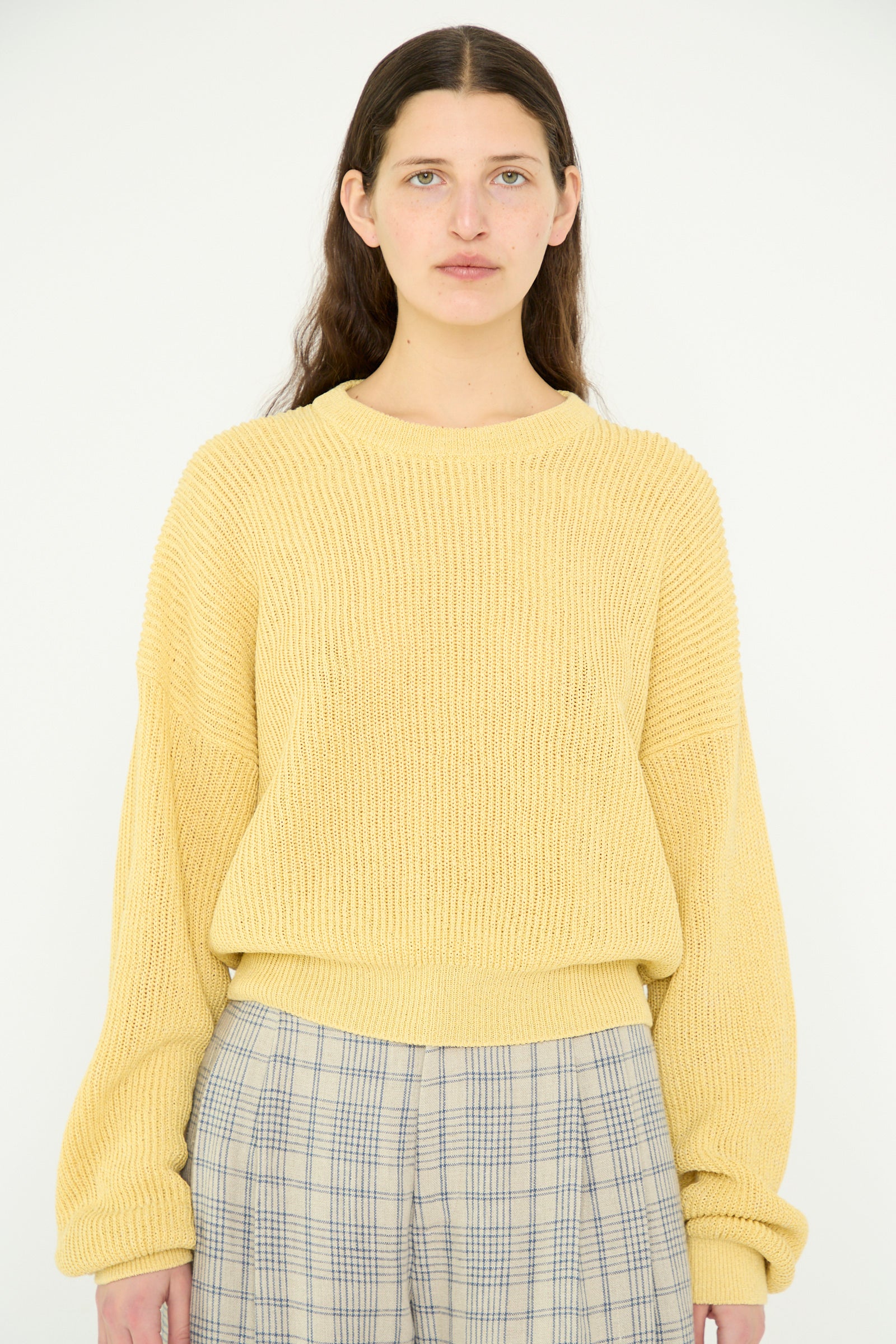 A model with long brown hair is wearing the Cristaseya Washi Paper Dropshoulder Cropped Sweater in Yellow and plaid pants, standing in front of a plain white background.