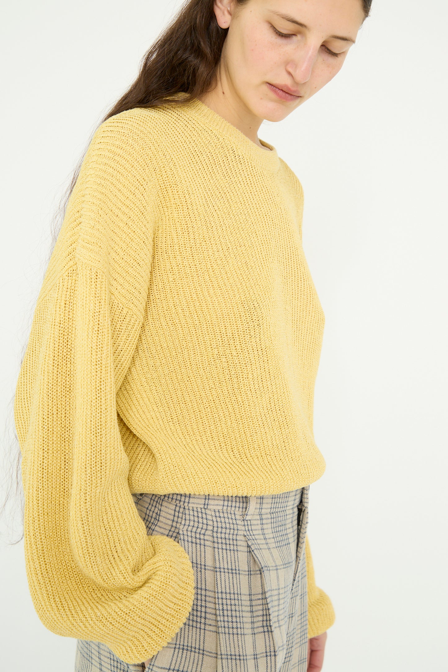 A person wearing the Cristaseya Washi Paper Dropshoulder Cropped Sweater in Yellow paired with plaid pants, looking down against a light background.