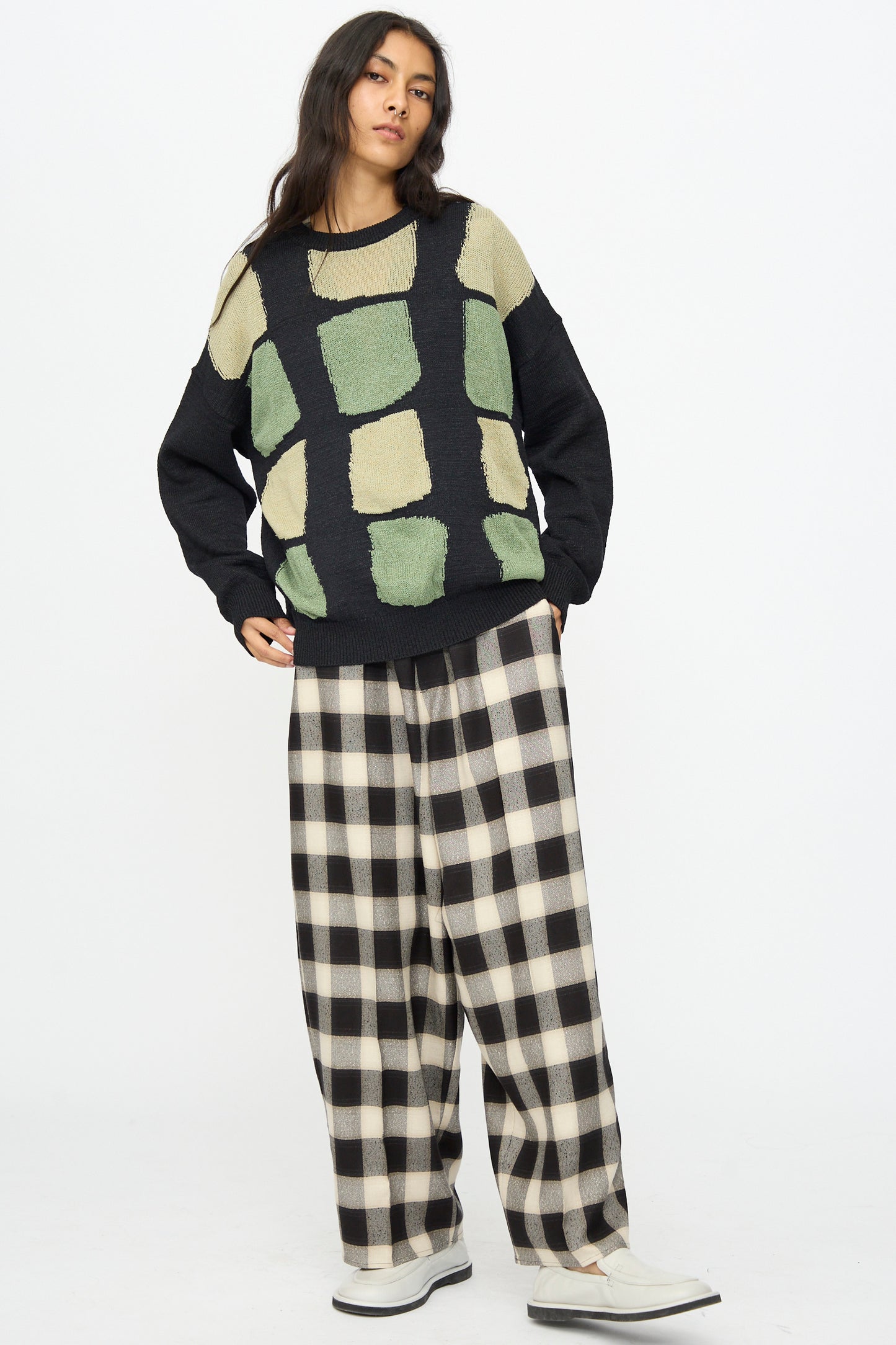 A person stands against a white background, wearing the Cristaseya Washi Paper Patchwork Sweater in Black with Sage and Light Khaki.