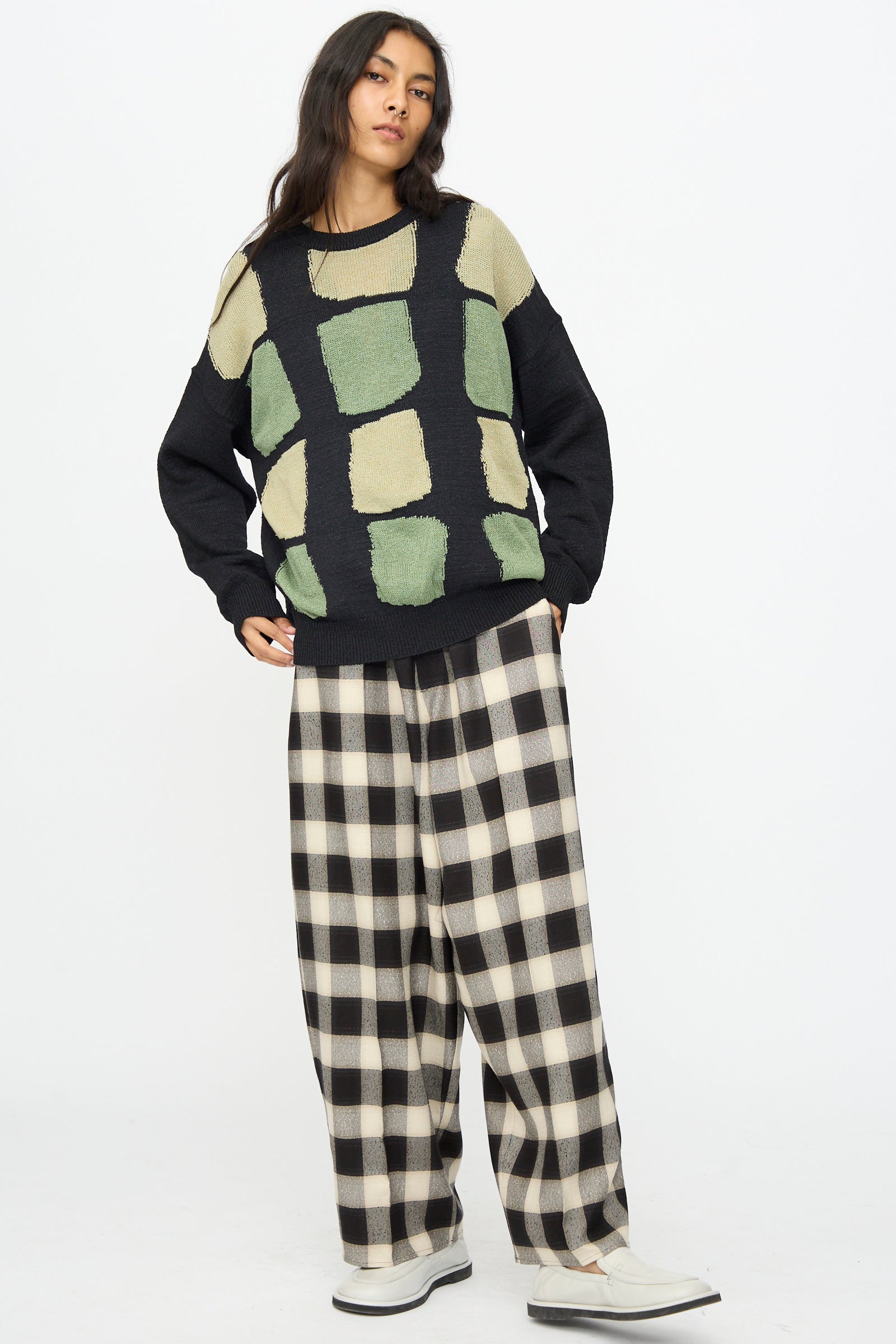 A person stands against a white background, wearing the Cristaseya Washi Paper Patchwork Sweater in Black with Sage and Light Khaki.