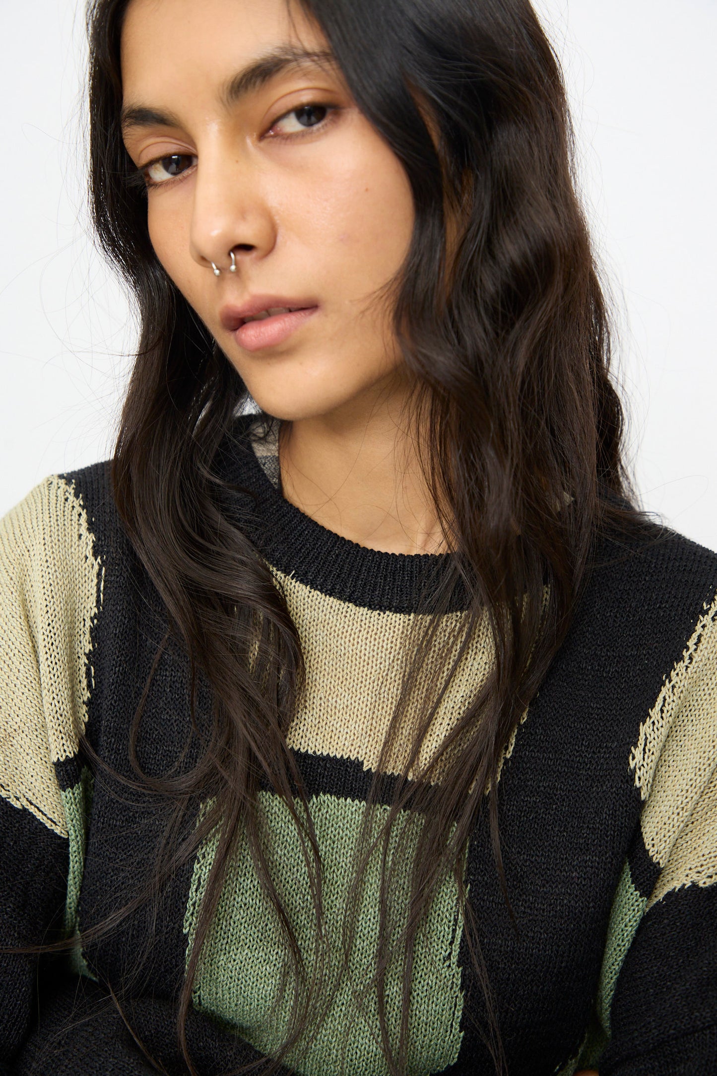 A person with long dark hair and a nose ring wears the Cristaseya Washi Paper Patchwork Sweater in Black with Sage and Light Khaki, looking toward the camera.