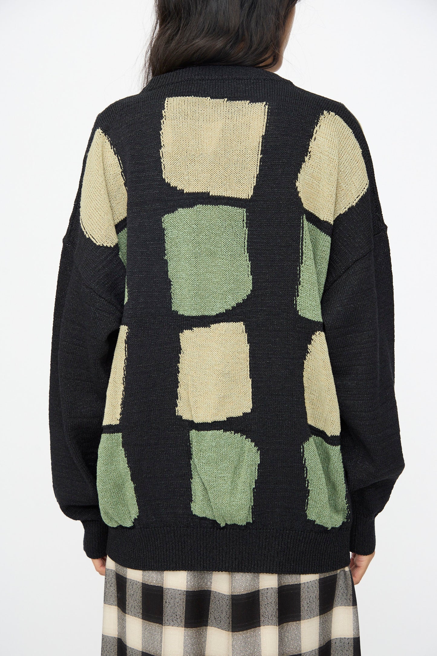 A person wears the Cristaseya Washi Paper Patchwork Sweater in Black with Sage and Light Khaki, paired with a black and white checkered skirt.